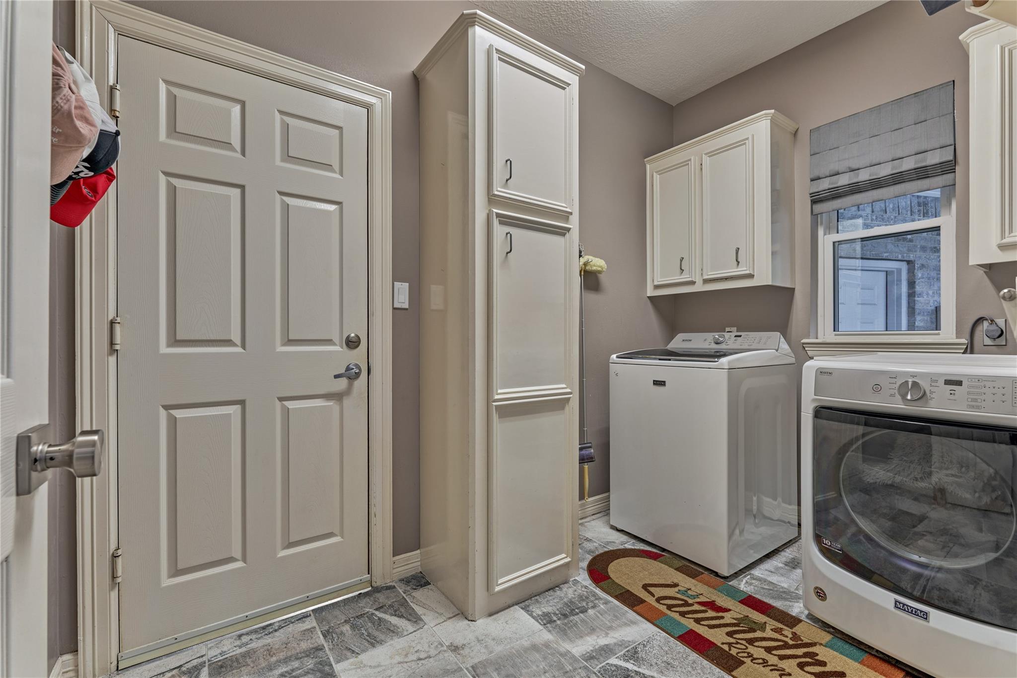 Laundry room with white cabinets, washer and dryer, gray tile floor, and a colorful floor mat.
