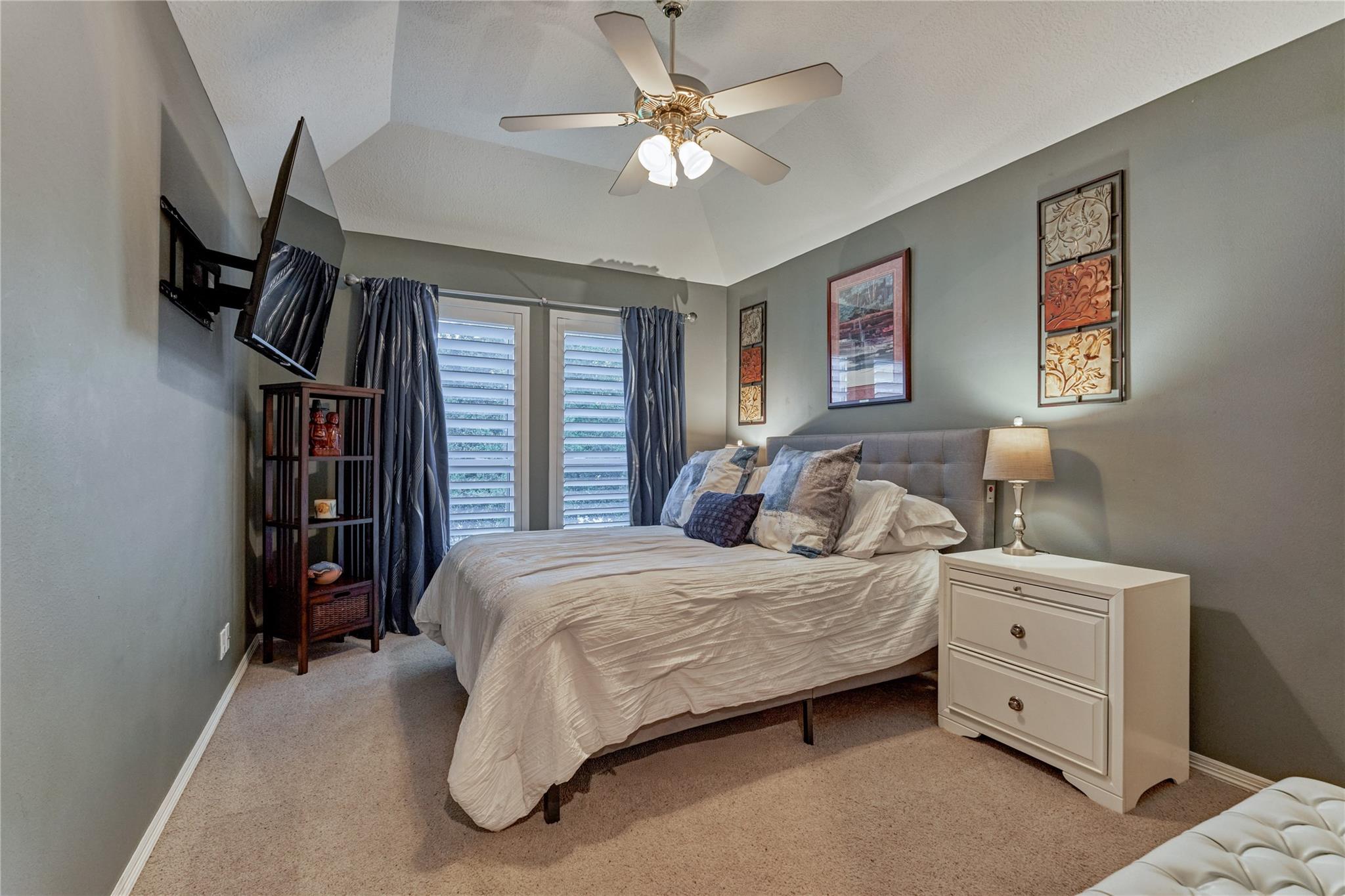 Bedroom with a large bed, shuttered windows, dark curtains, and a ceiling fan.