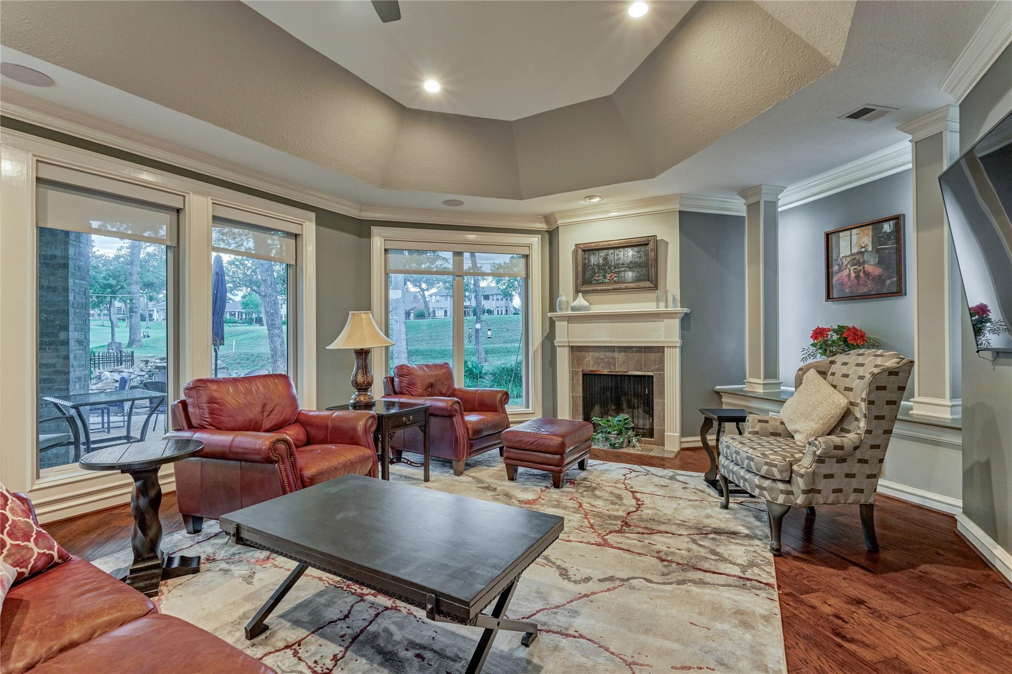 Living room with a fireplace, red leather seating, and large windows overlooking a lawn.