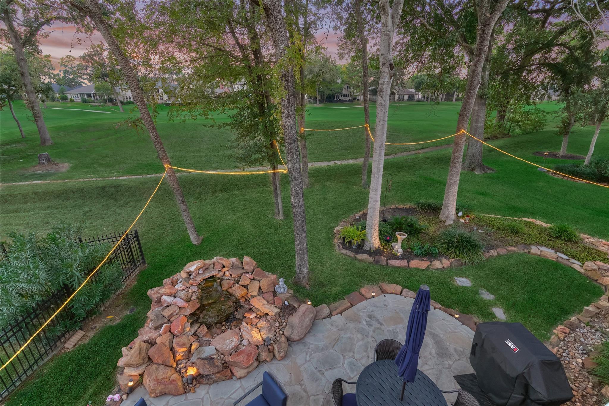 Stone patio and rock waterfall overlook a tree-lined lawn and golf course.