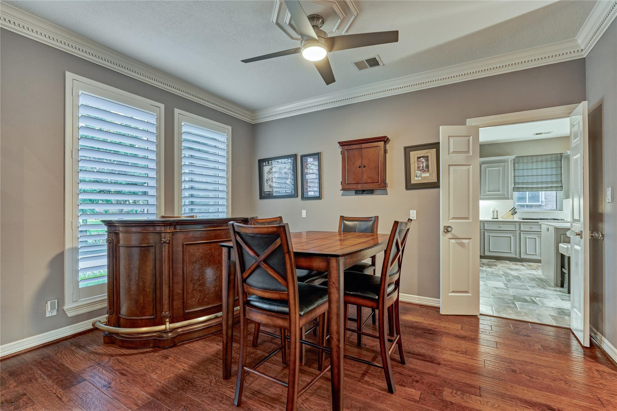 Dining room with dark wood furniture, plantation shutters, and an open doorway to the kitchen.