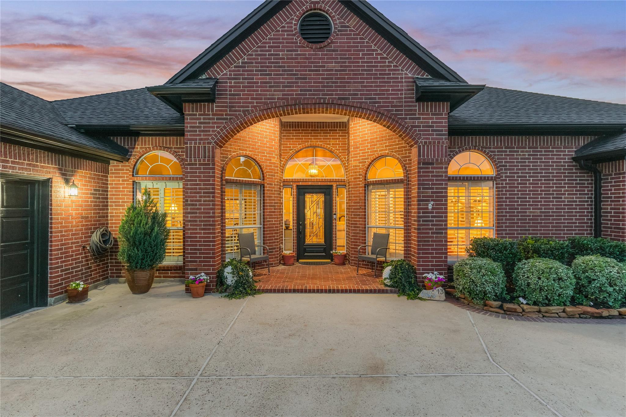 Red-brick home with a tall gabled entry, glowing arched windows, and a landscaped front porch.