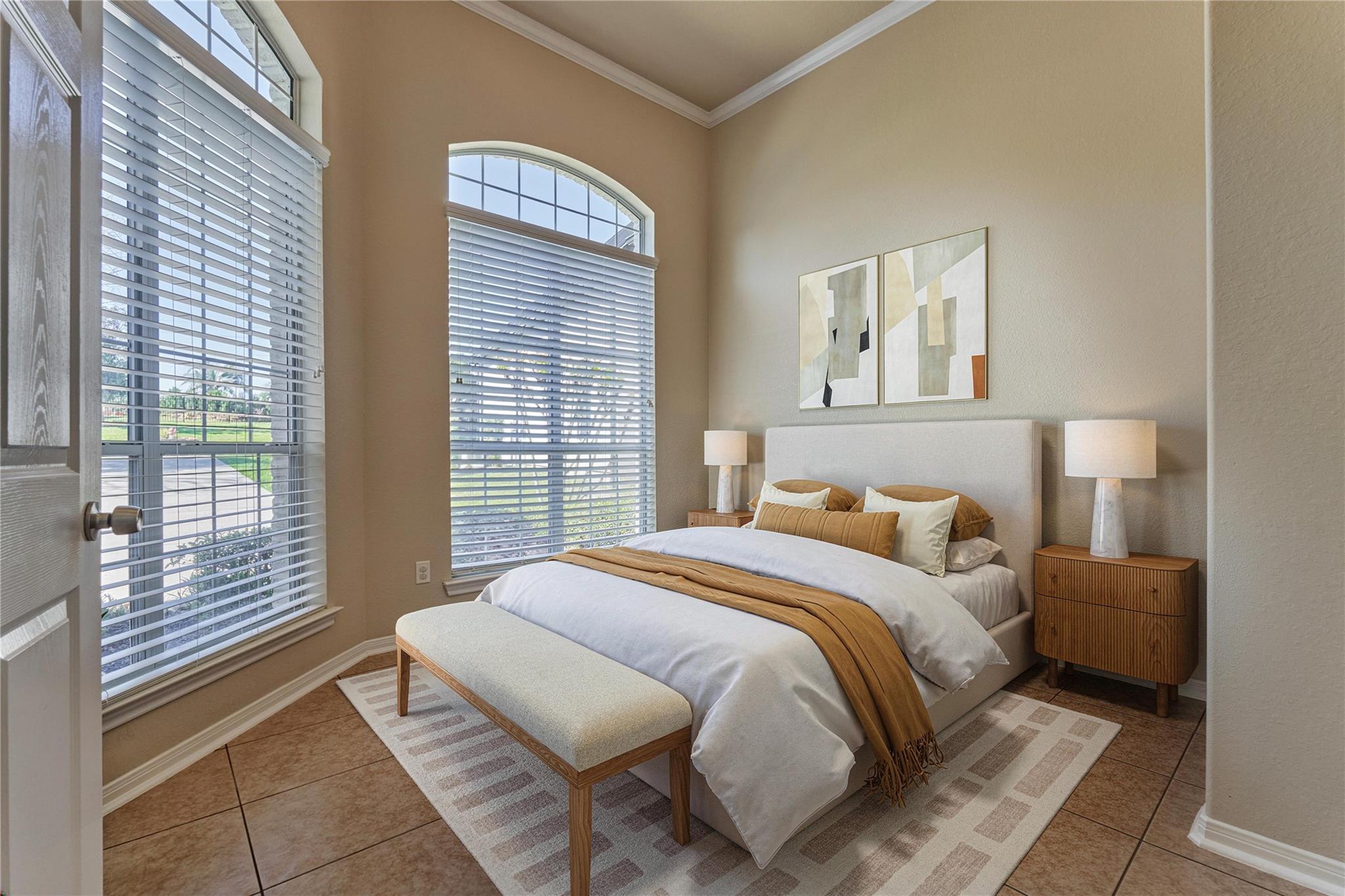 Staged bedroom with a large bed and bench beneath tall arched windows.