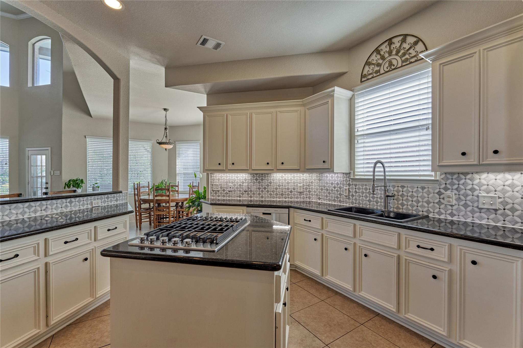 Kitchen with cream cabinets, patterned backsplash, and a central island with gas cooktop.