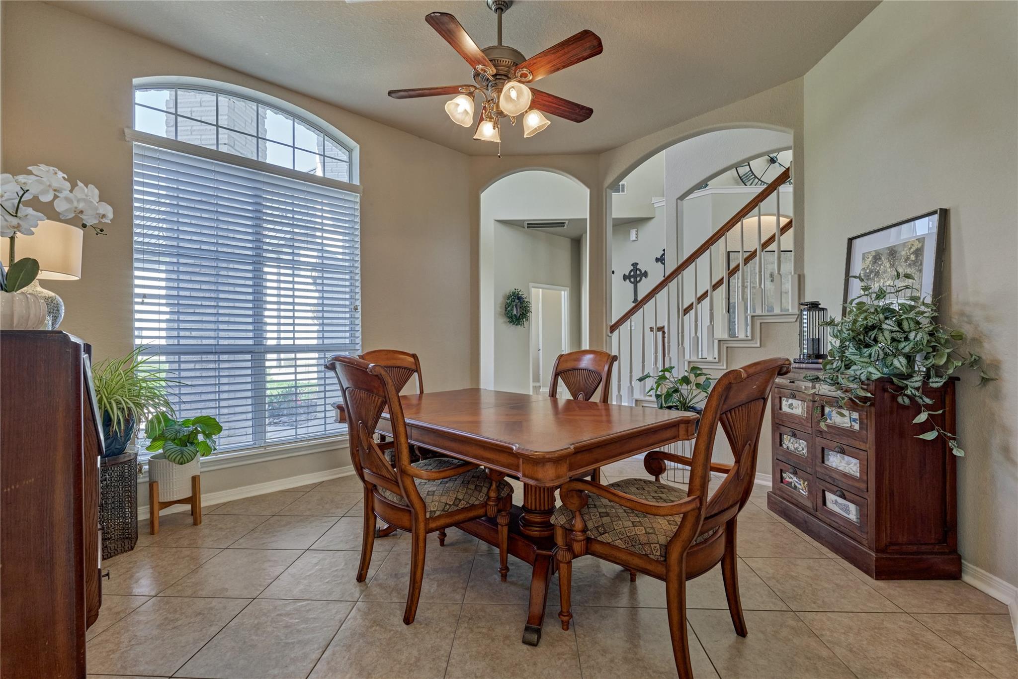 Dining room with a wooden table, arched window, and staircase beyond.