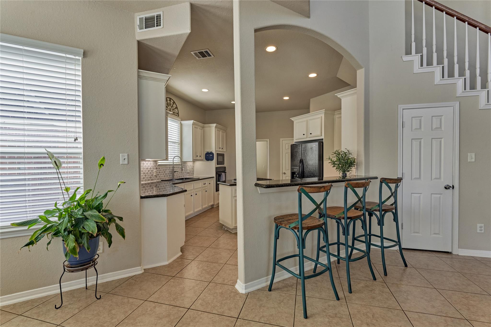 Kitchen with white cabinets and a breakfast bar lined with three stools beside the staircase.