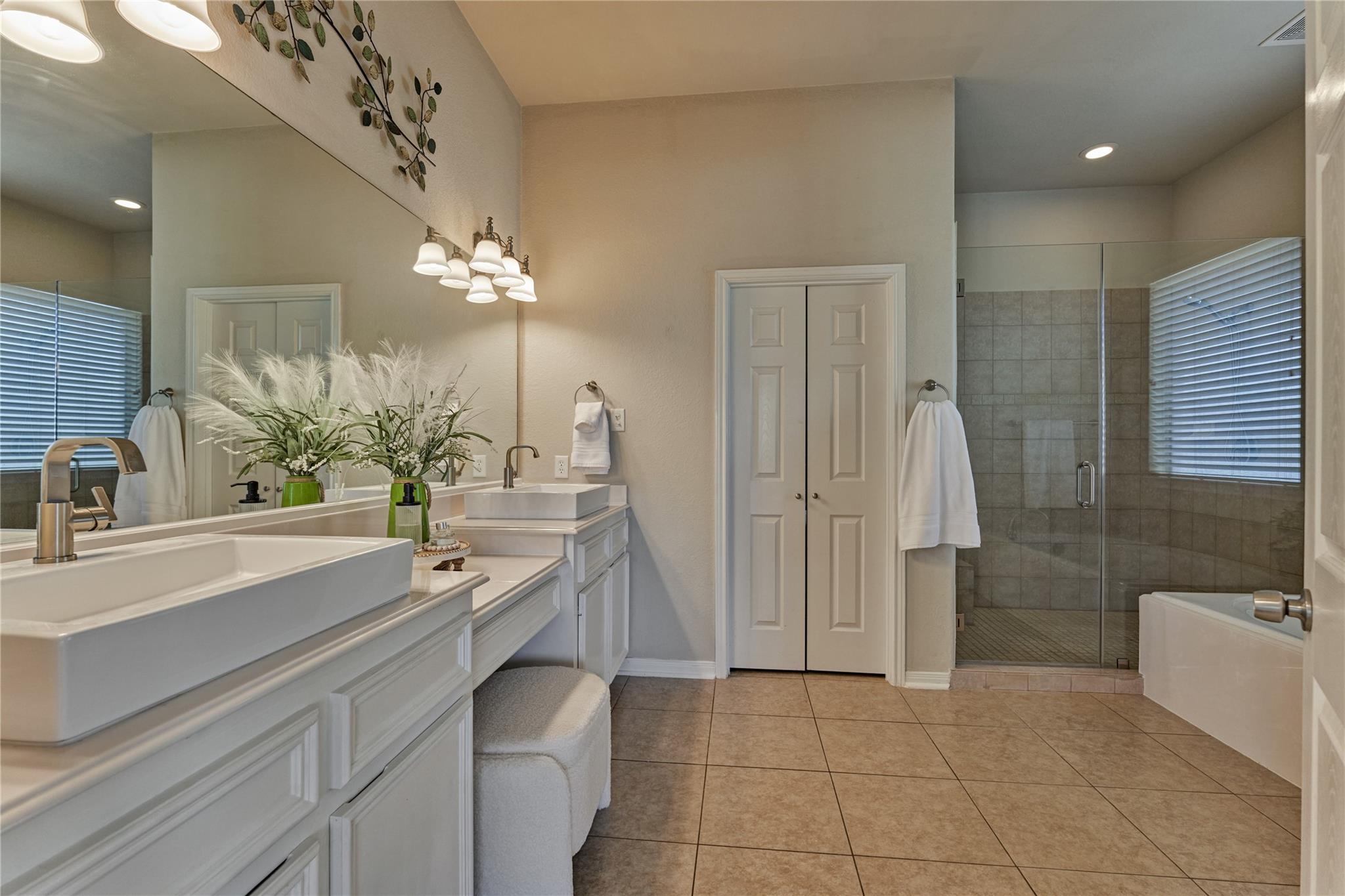 Primary bathroom with double vessel sinks, a glass-enclosed tiled shower, and a bathtub beside a window.