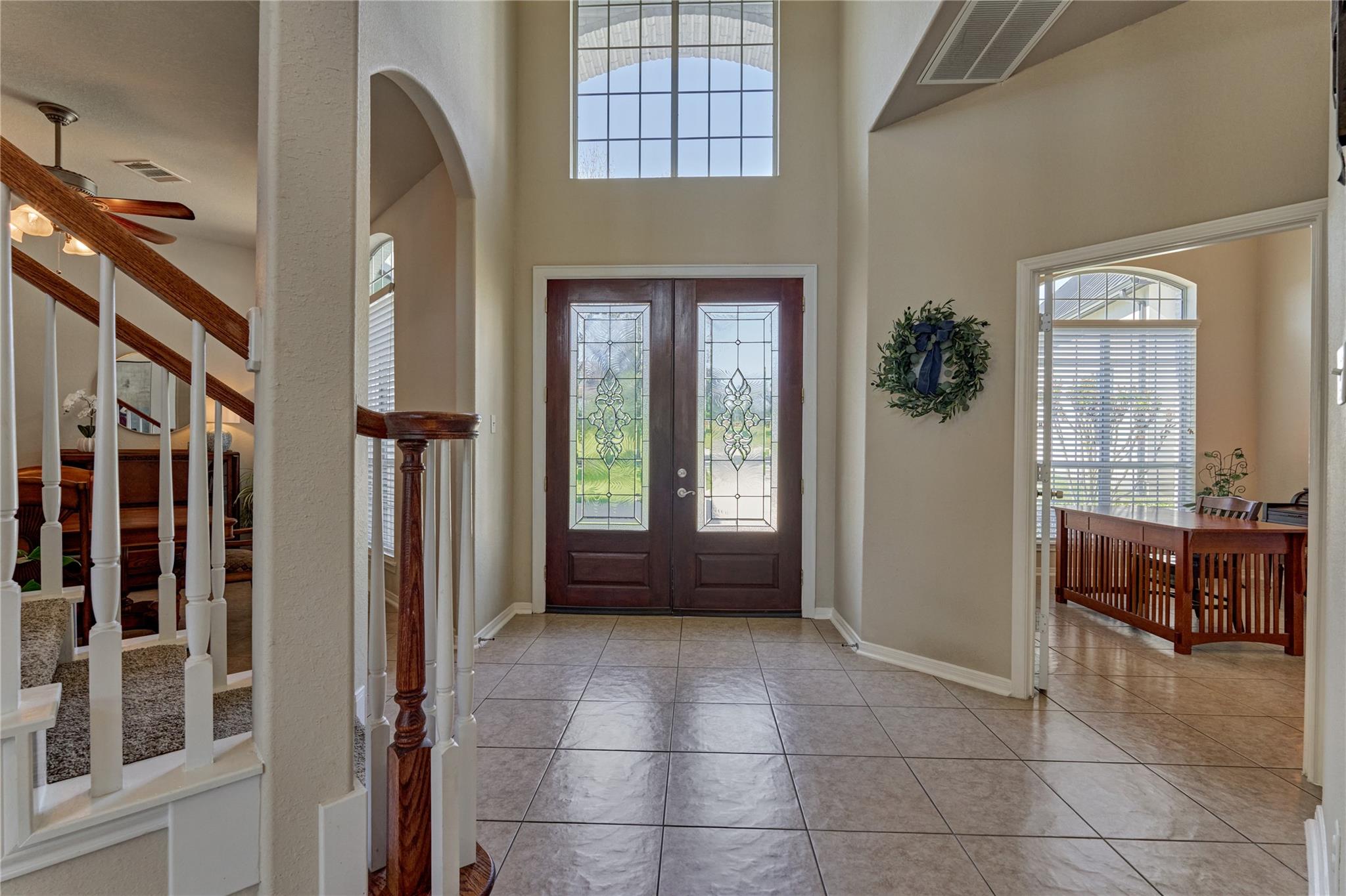 Home foyer with decorative glass double doors, a tall window, and a staircase beside the dining room.