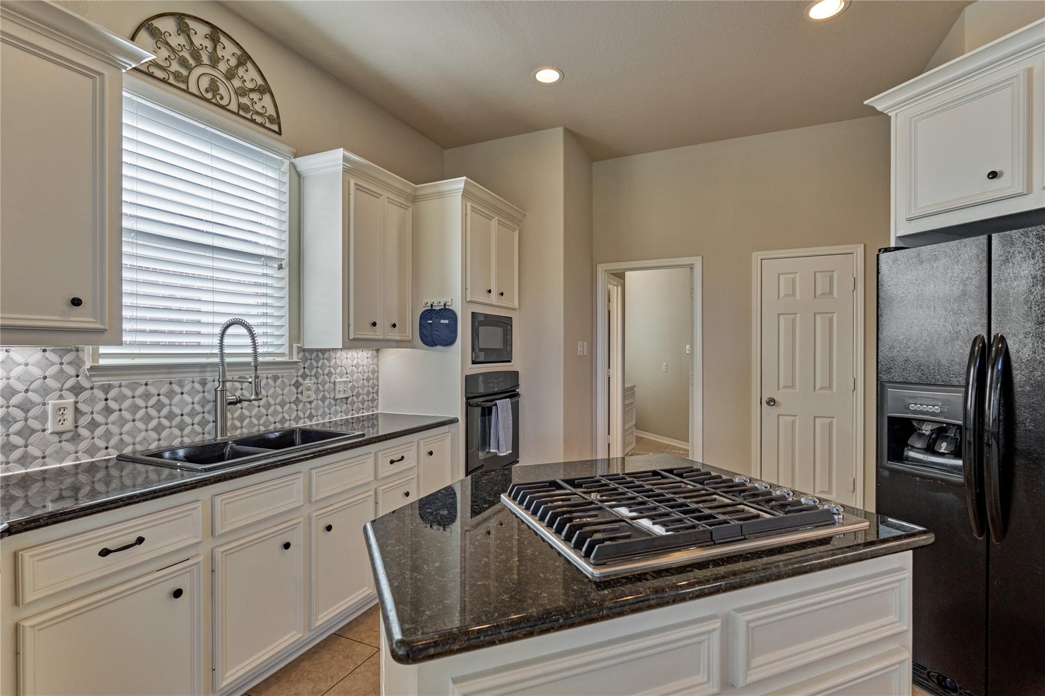 Kitchen with white cabinets, patterned tile backsplash, and a large granite island with a gas cooktop.