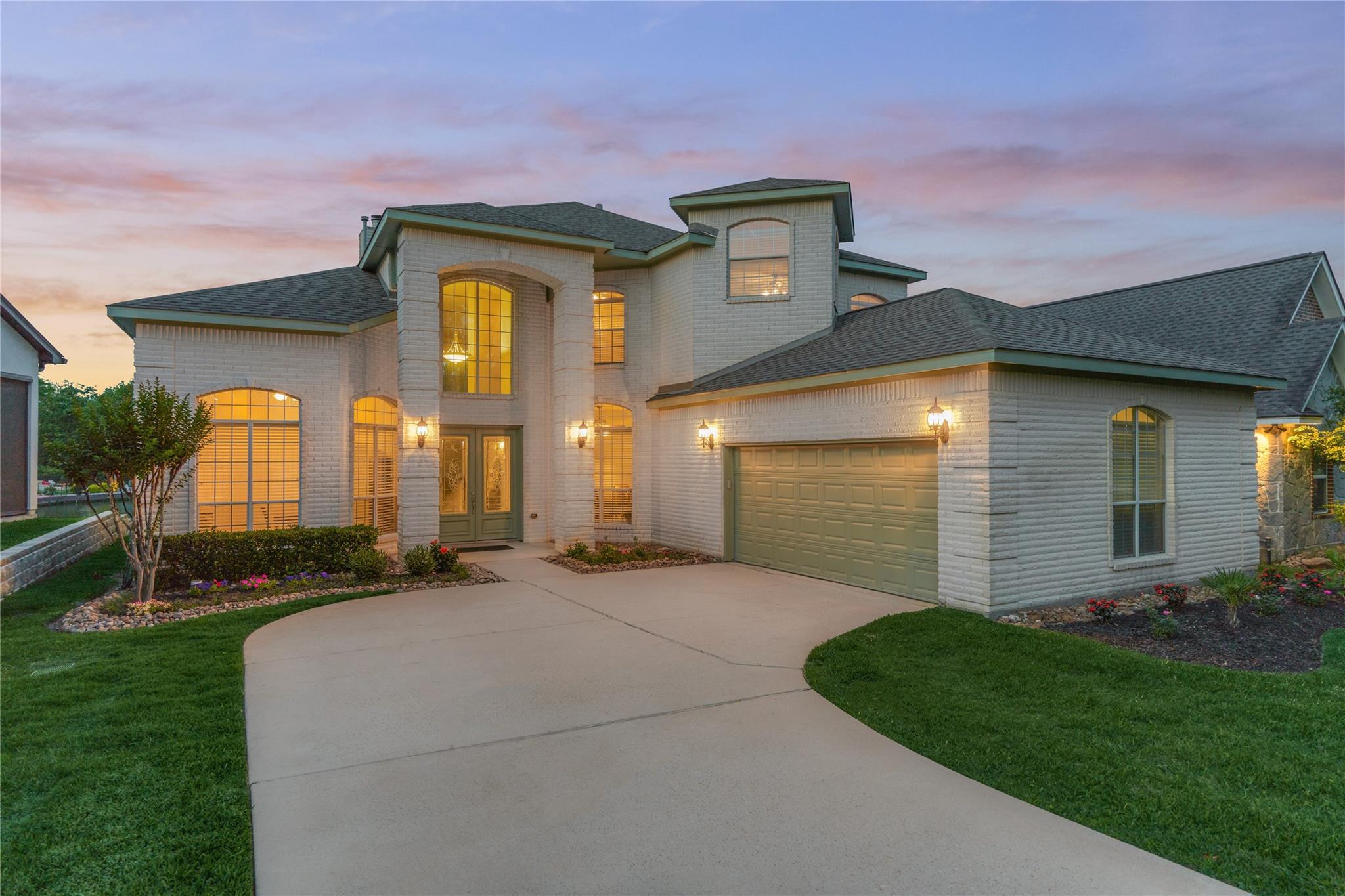 Two-story brick home with illuminated windows, attached garage, and curved driveway at dusk.