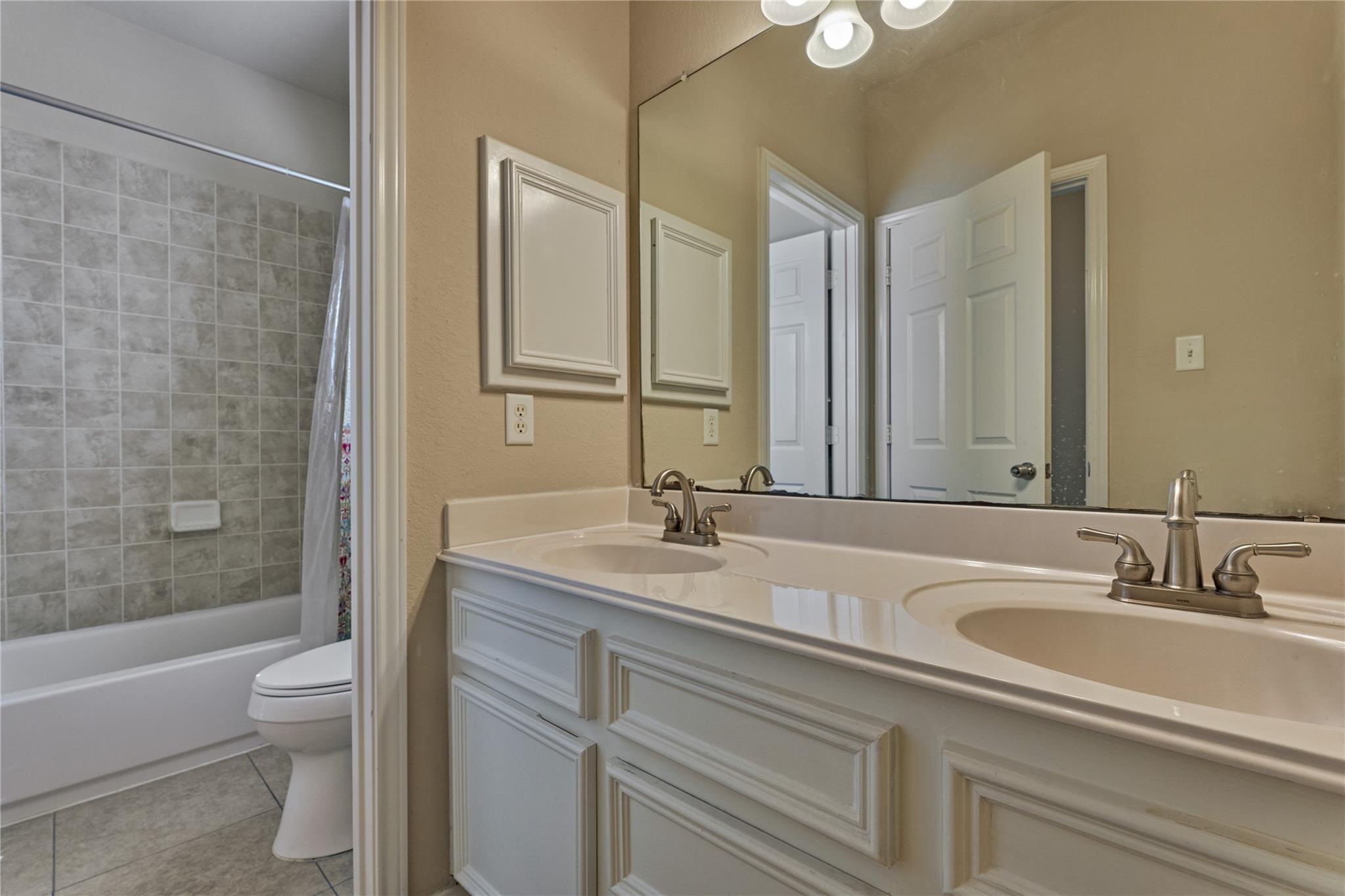 Bathroom with a double-sink vanity and tiled tub and shower beside the toilet.