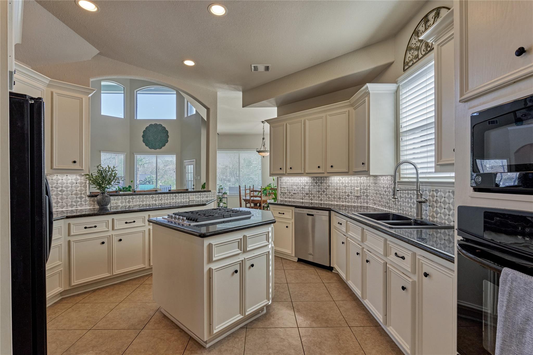 Kitchen with cream cabinets, patterned backsplash, and a central island with gas cooktop.