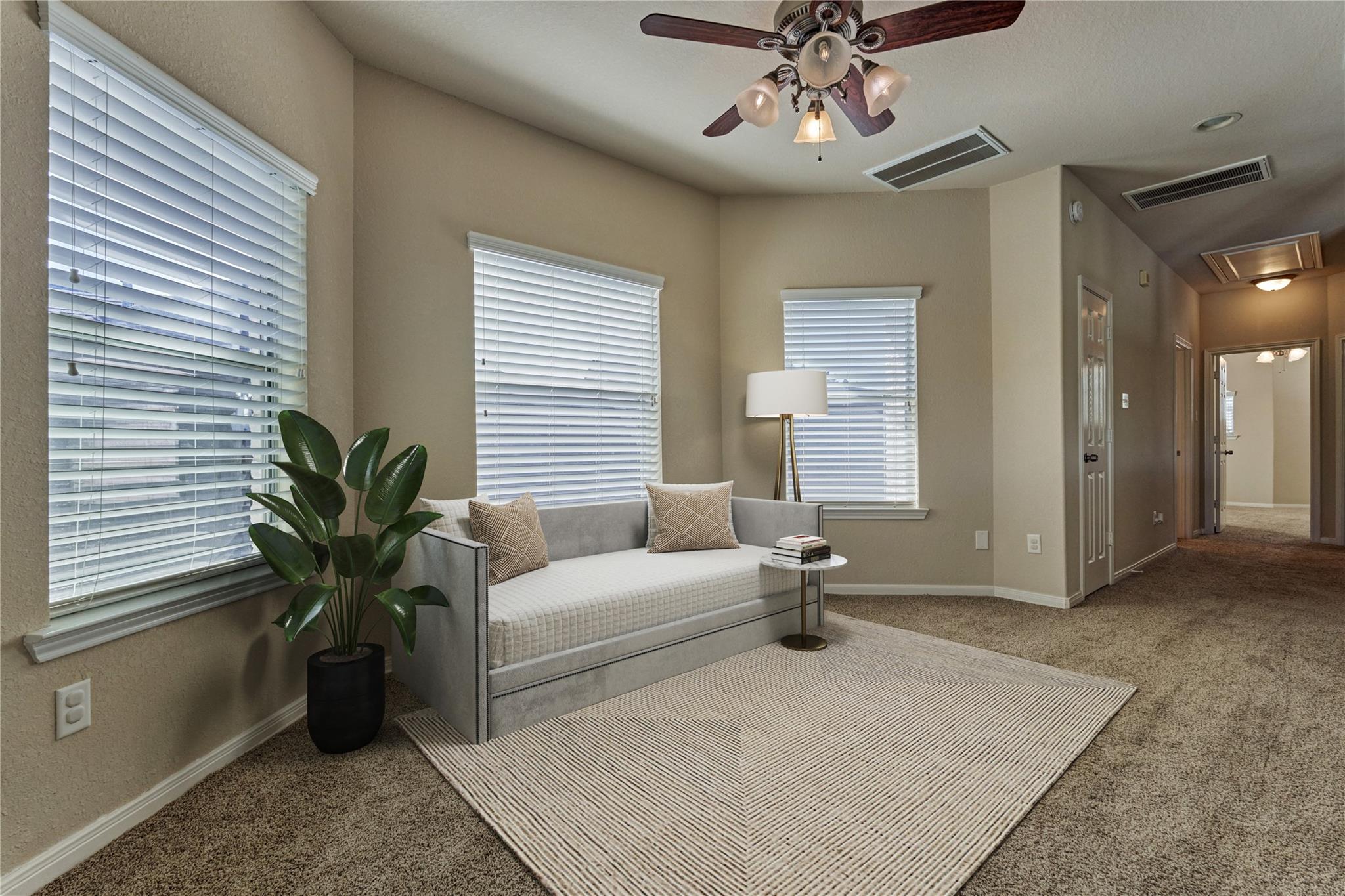Staged sitting room with a gray sofa, patterned rug, and windows with white blinds.