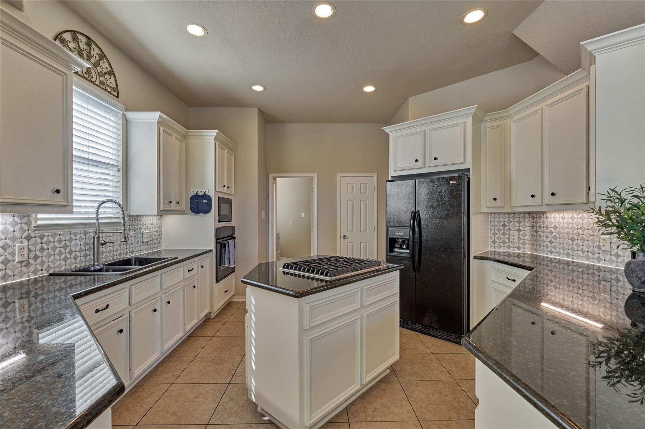 Kitchen with white cabinetry, patterned tile backsplash, dark granite counters, and a central cooktop island.