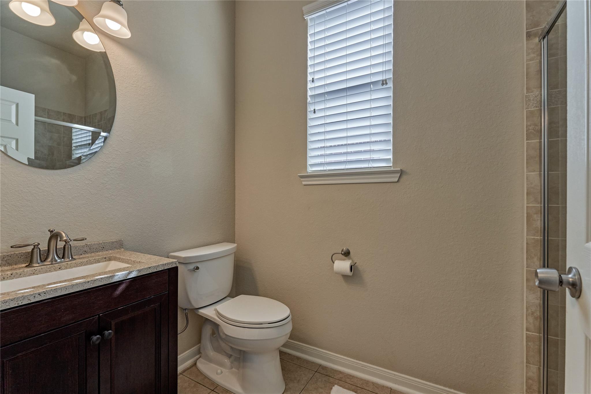 Bathroom with a dark wood vanity, toilet beneath a window, and tiled glass-enclosed shower.