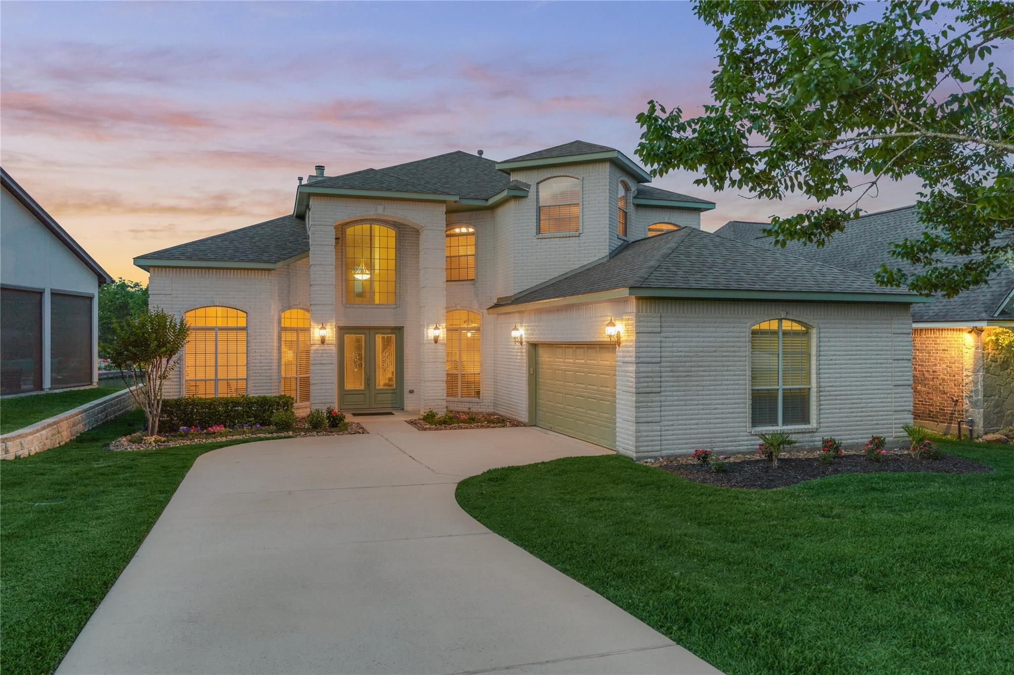 Two-story brick house with glowing arched windows, an attached garage, and a curved driveway at dusk.