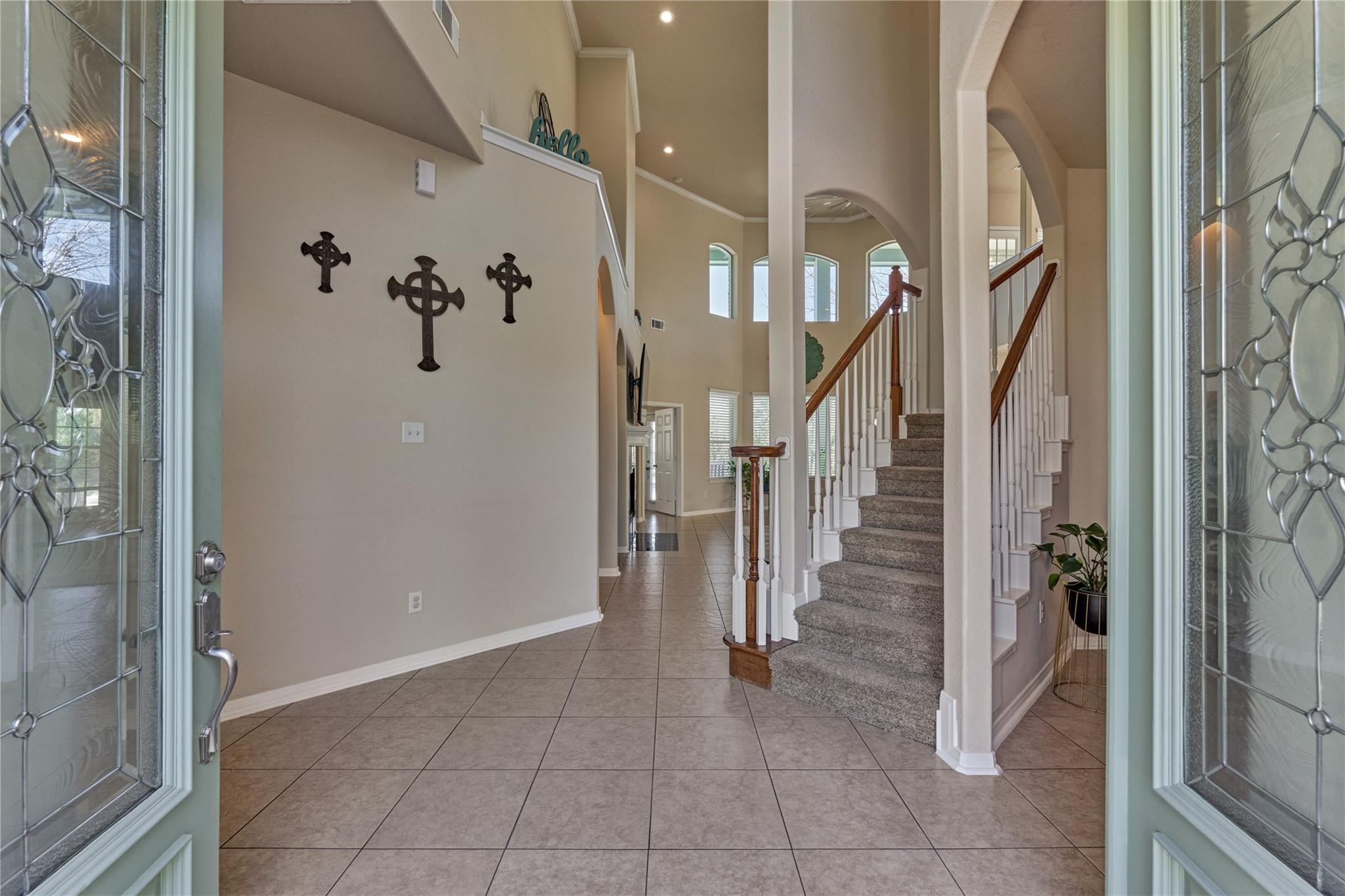 Foyer with tiled floors, arched openings, and a carpeted staircase with a wood handrail.