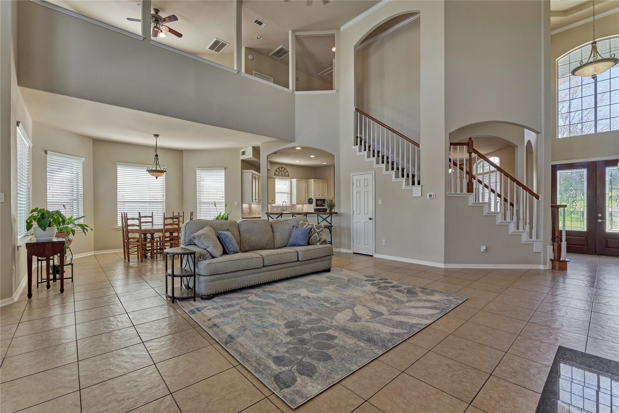 Open-concept living room with a gray sofa, tiled floors, tall windows, and two staircases.