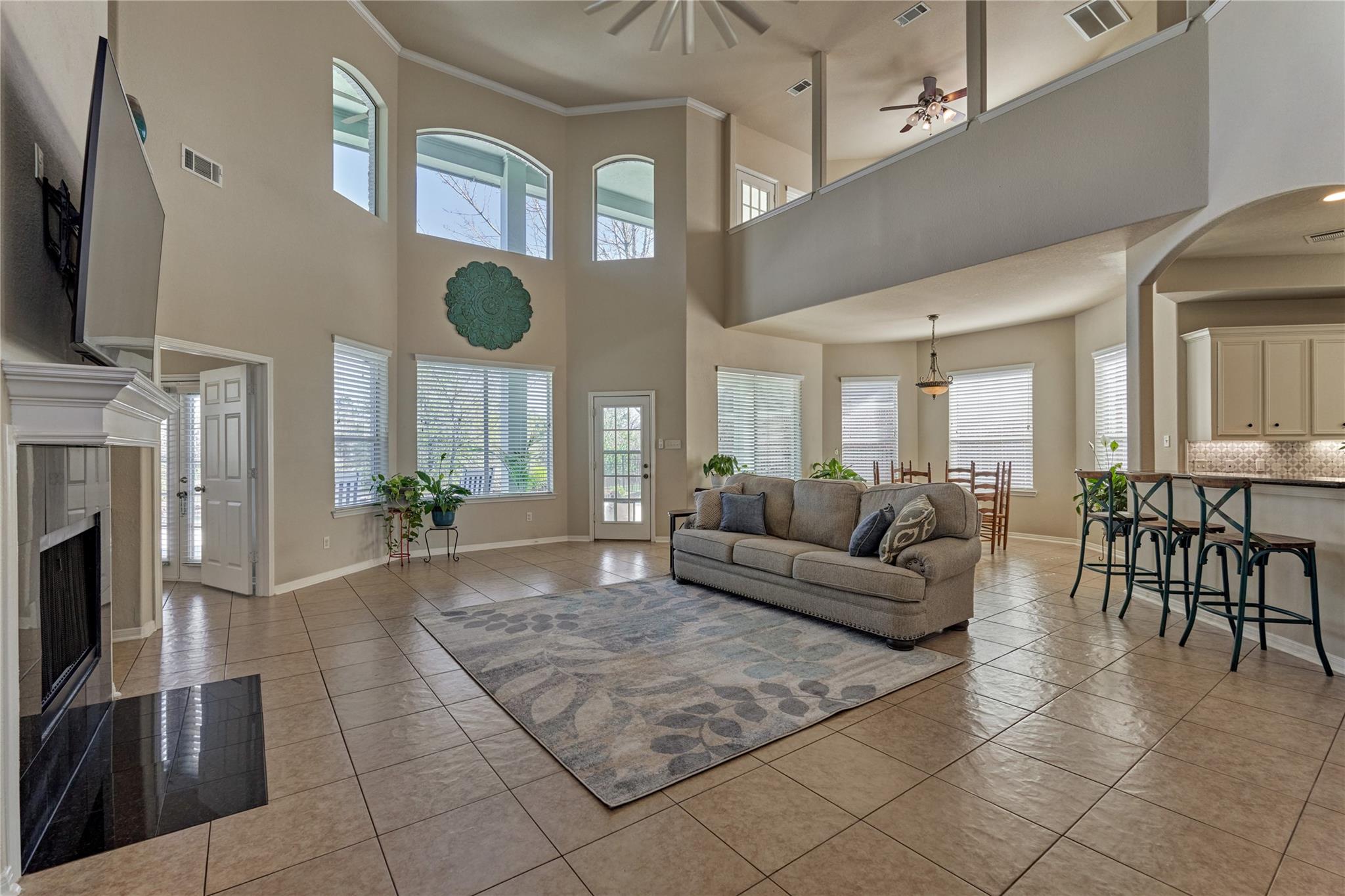 Open-plan living room with a tall ceiling, arched windows, tiled floors, and fireplace.