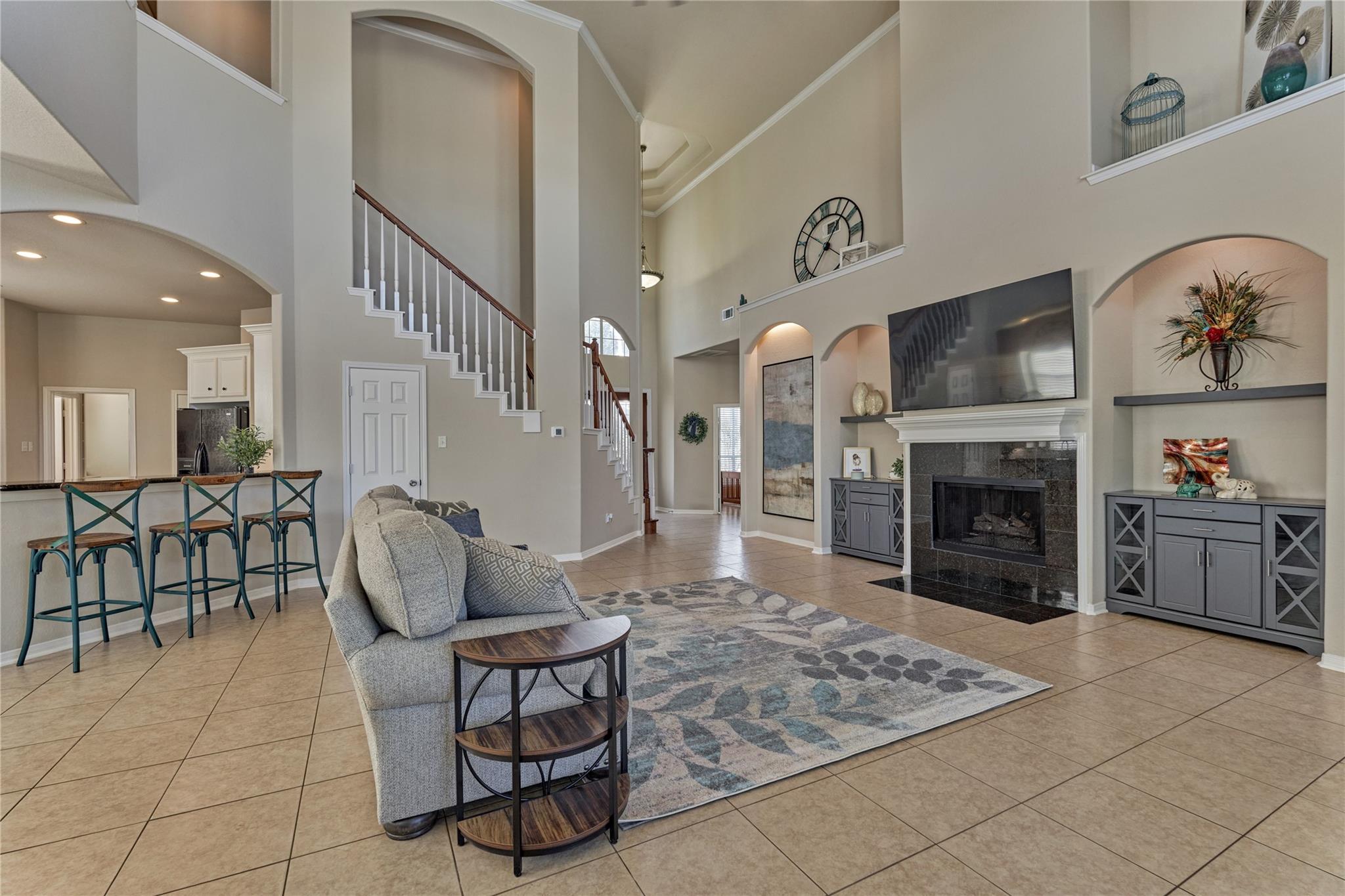 Two-story living room with a tiled floor, staircase, fireplace, and breakfast bar.