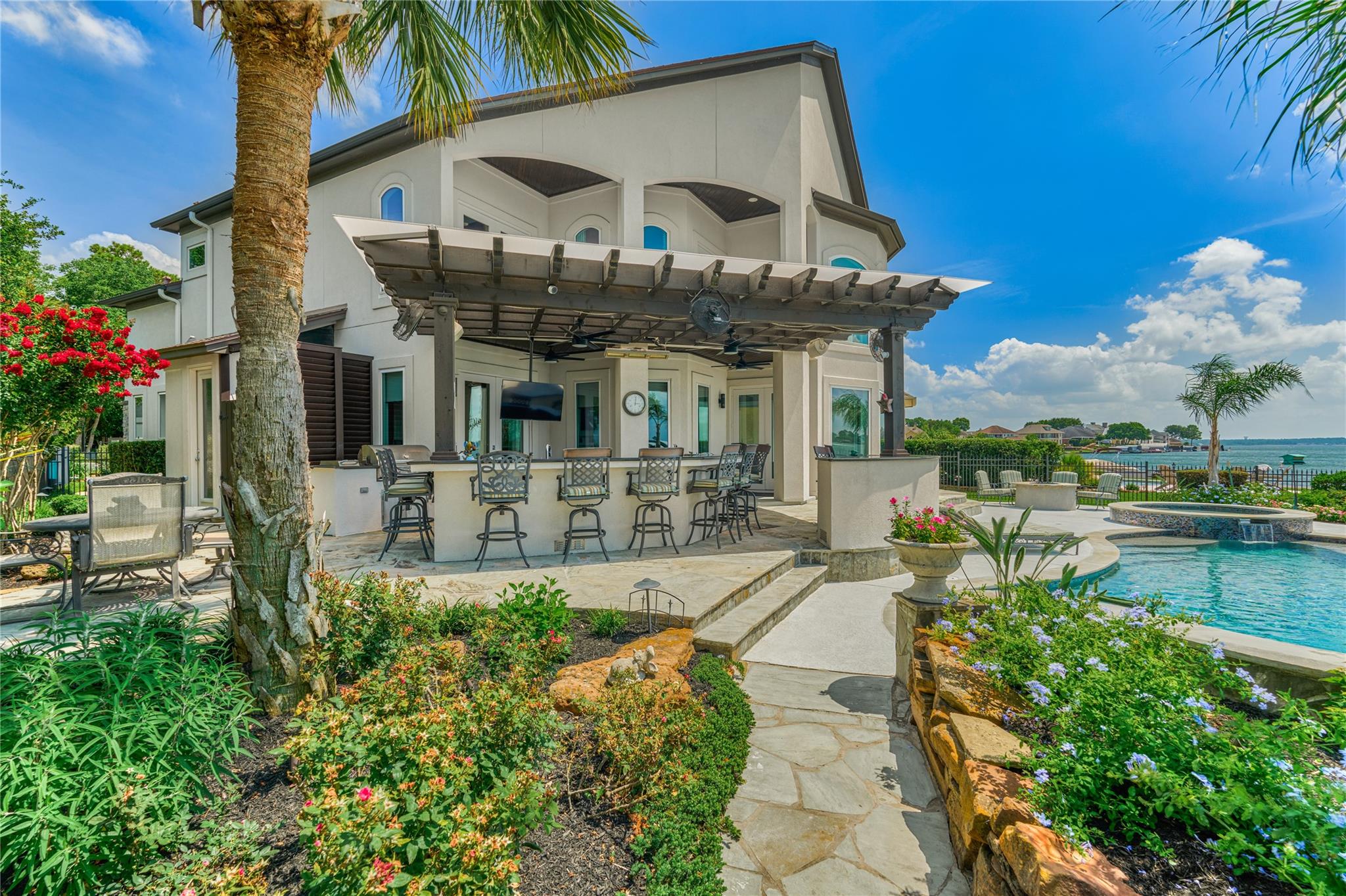 Waterfront home with a covered outdoor bar beside a landscaped pool patio.