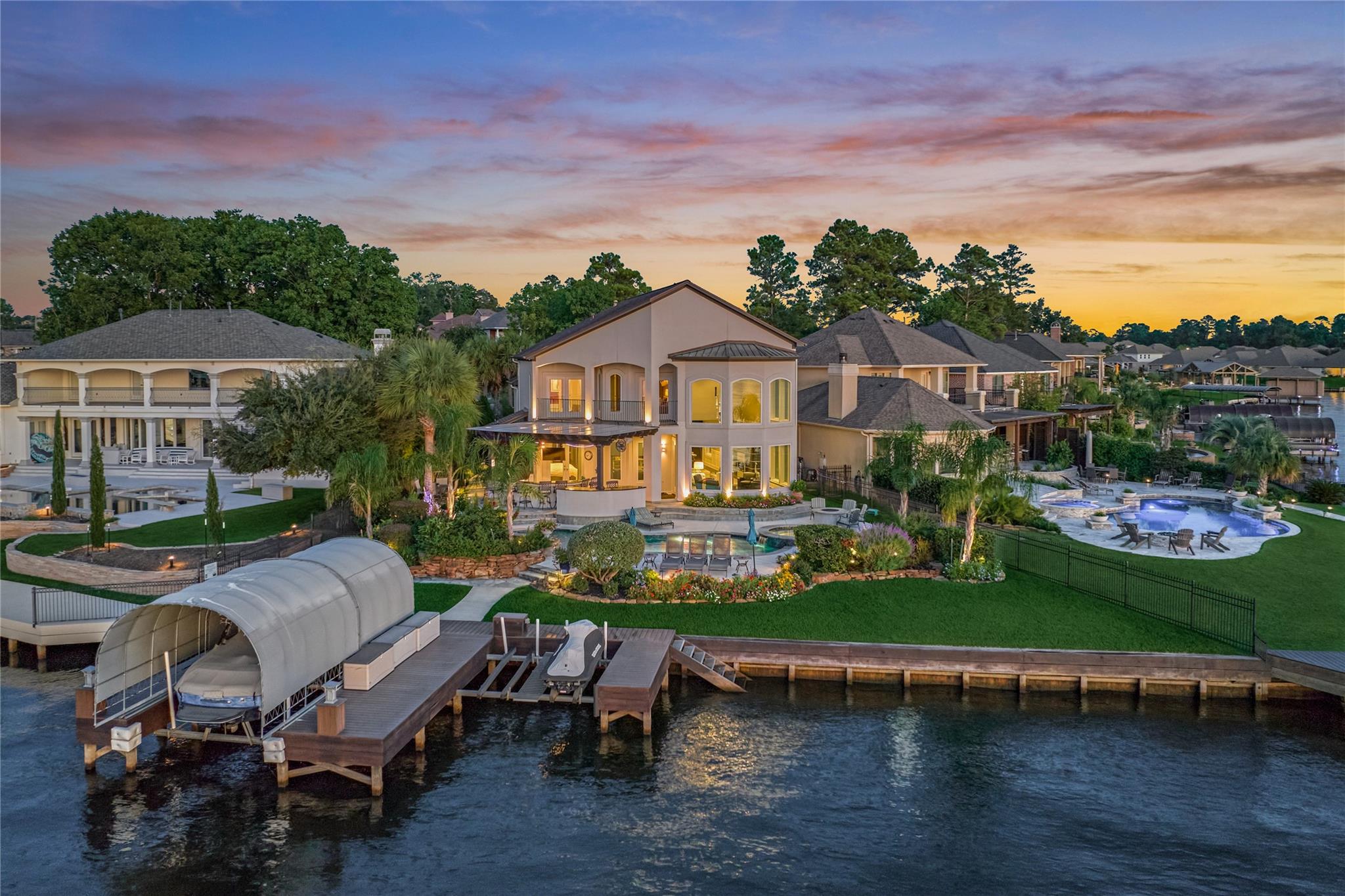 Two-story waterfront home with a pool, landscaped yard, and covered boat lift at dusk.