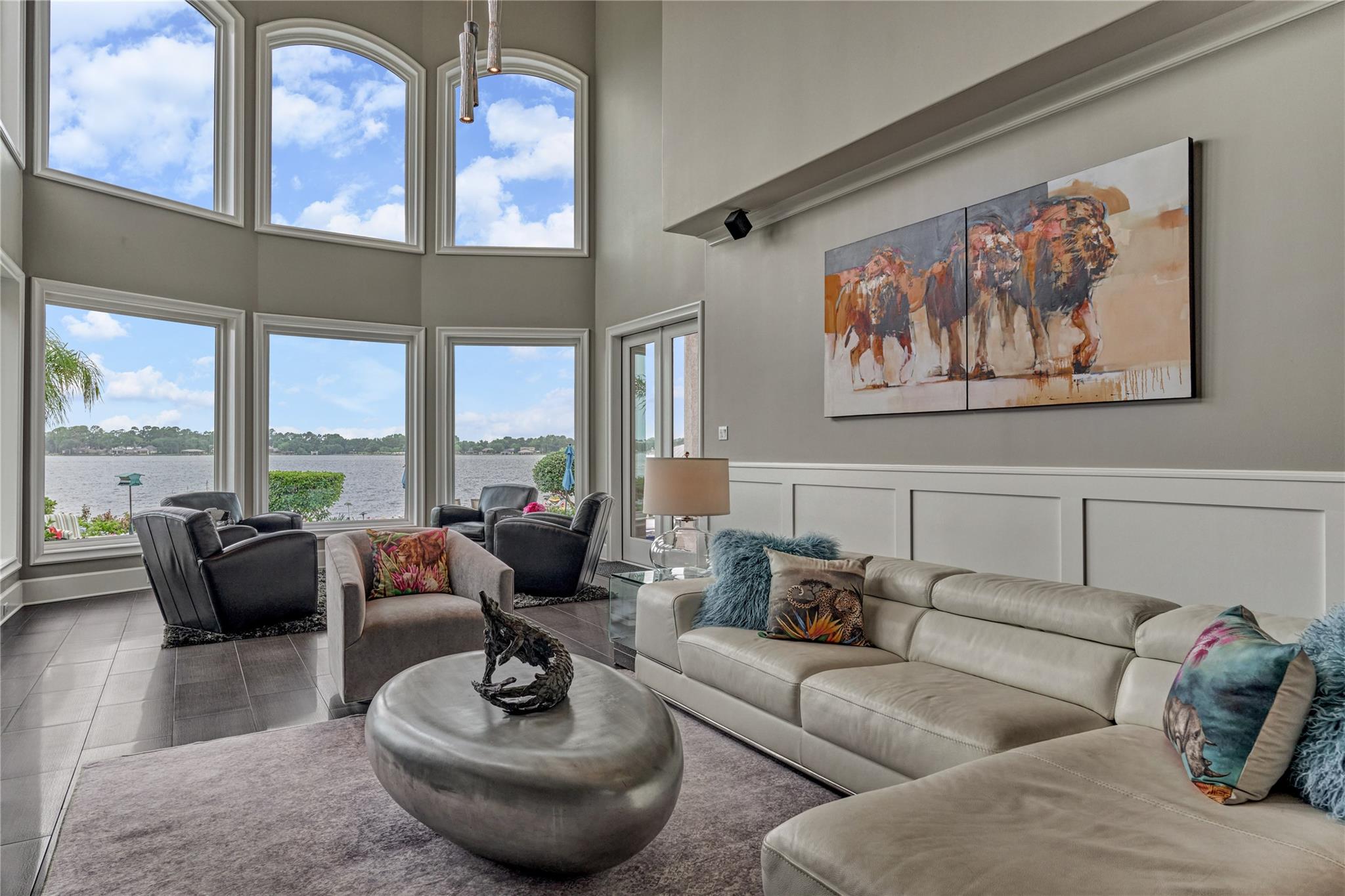 Lakefront living room with soaring windows, a cream sectional, and dark lounge chairs.