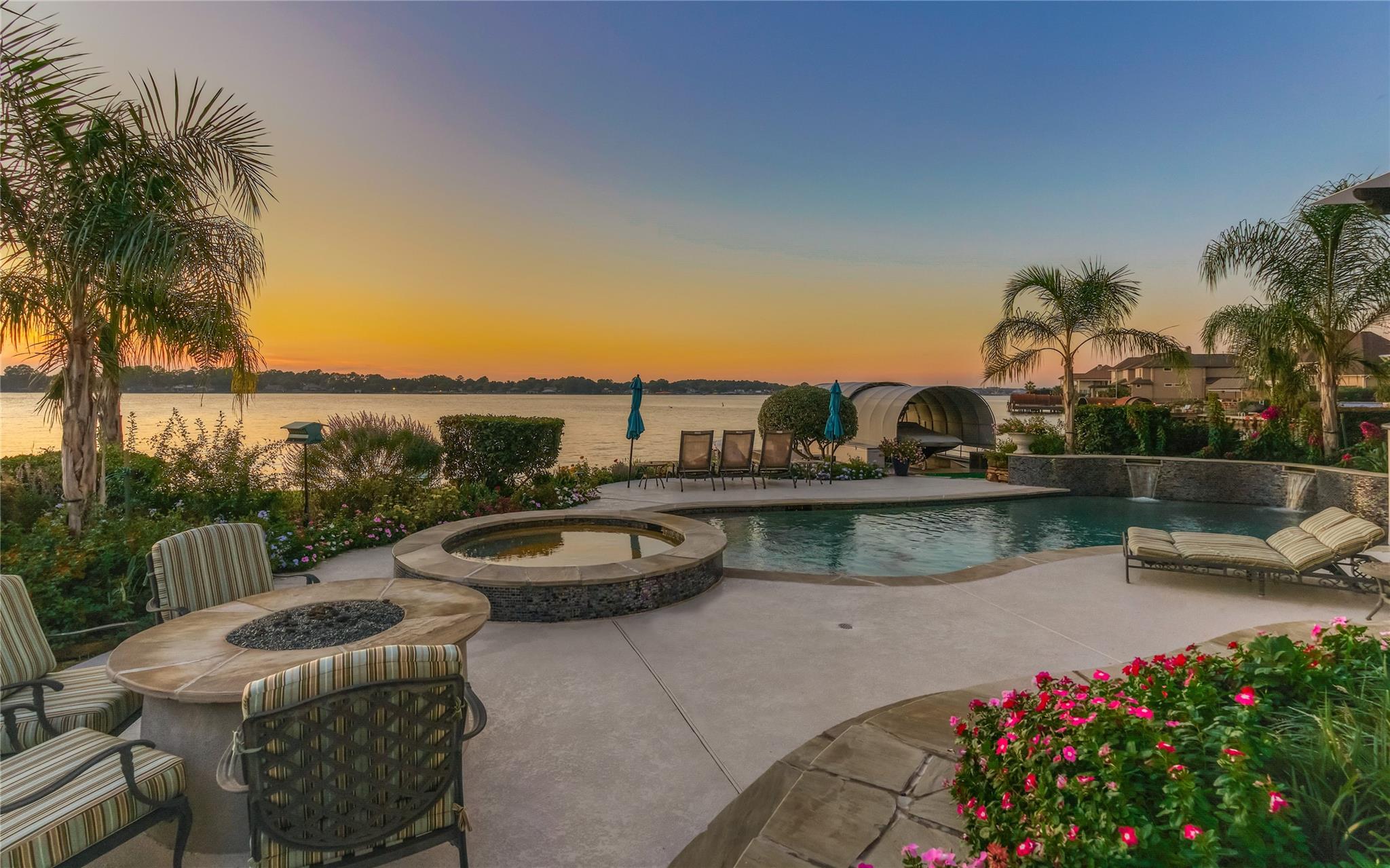 Waterfront backyard with a pool, circular spa, and furnished patio overlooking the lake at sunset.