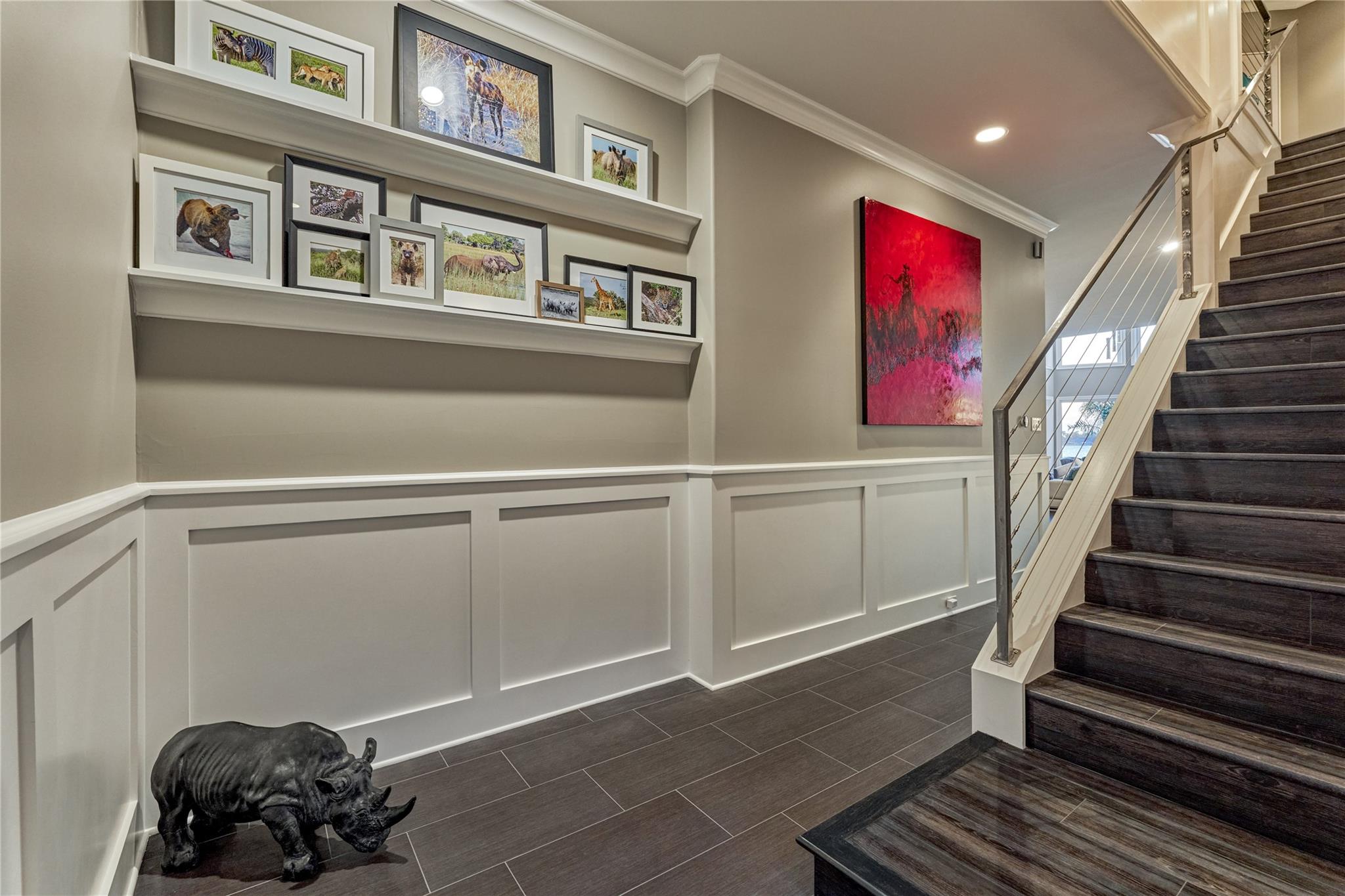 Entry hall with dark wood stairs, cable railing, and shelves of framed wildlife photographs.