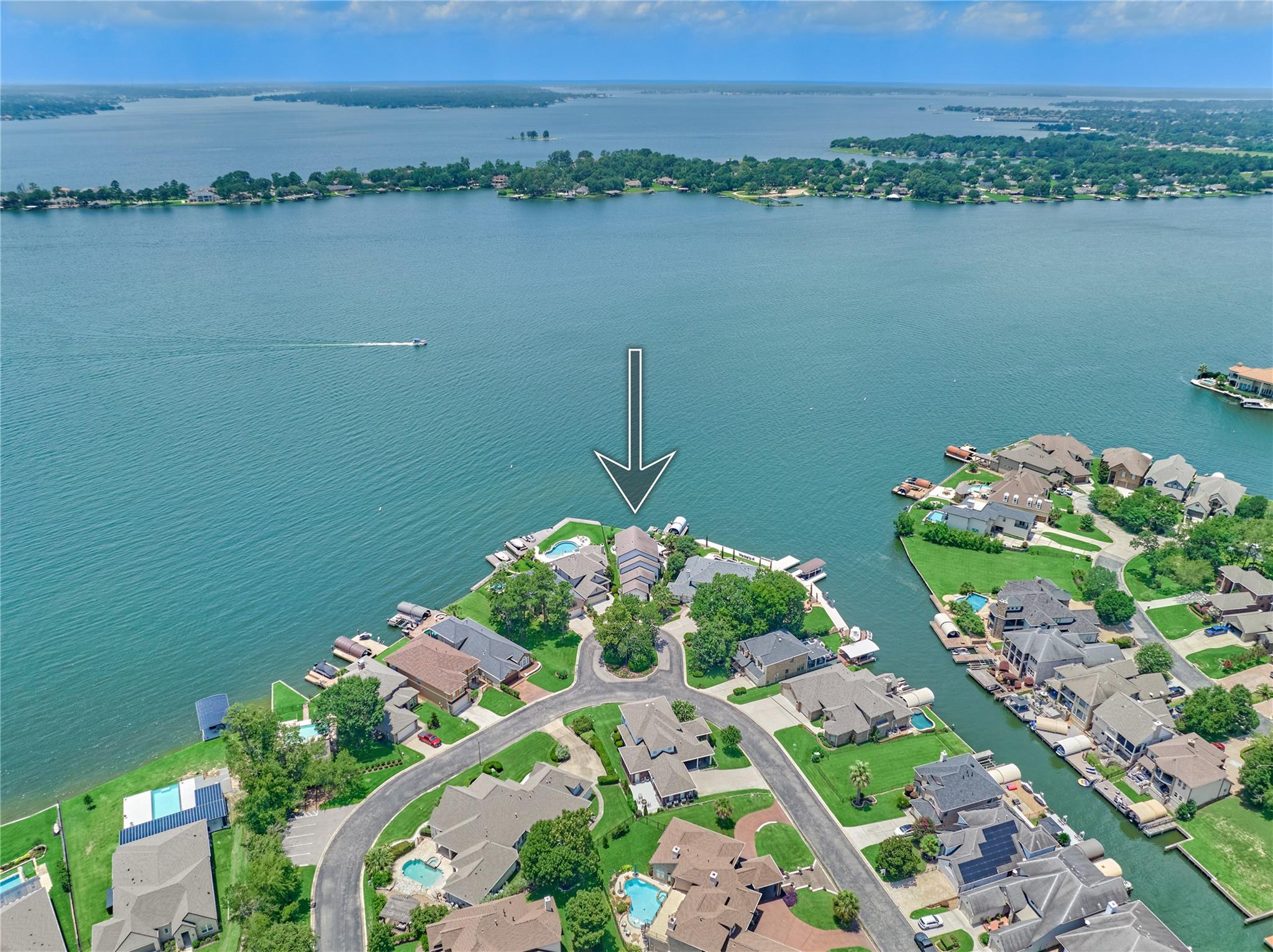 Aerial view of an arrow-marked lakefront home with a pool and surrounding water.