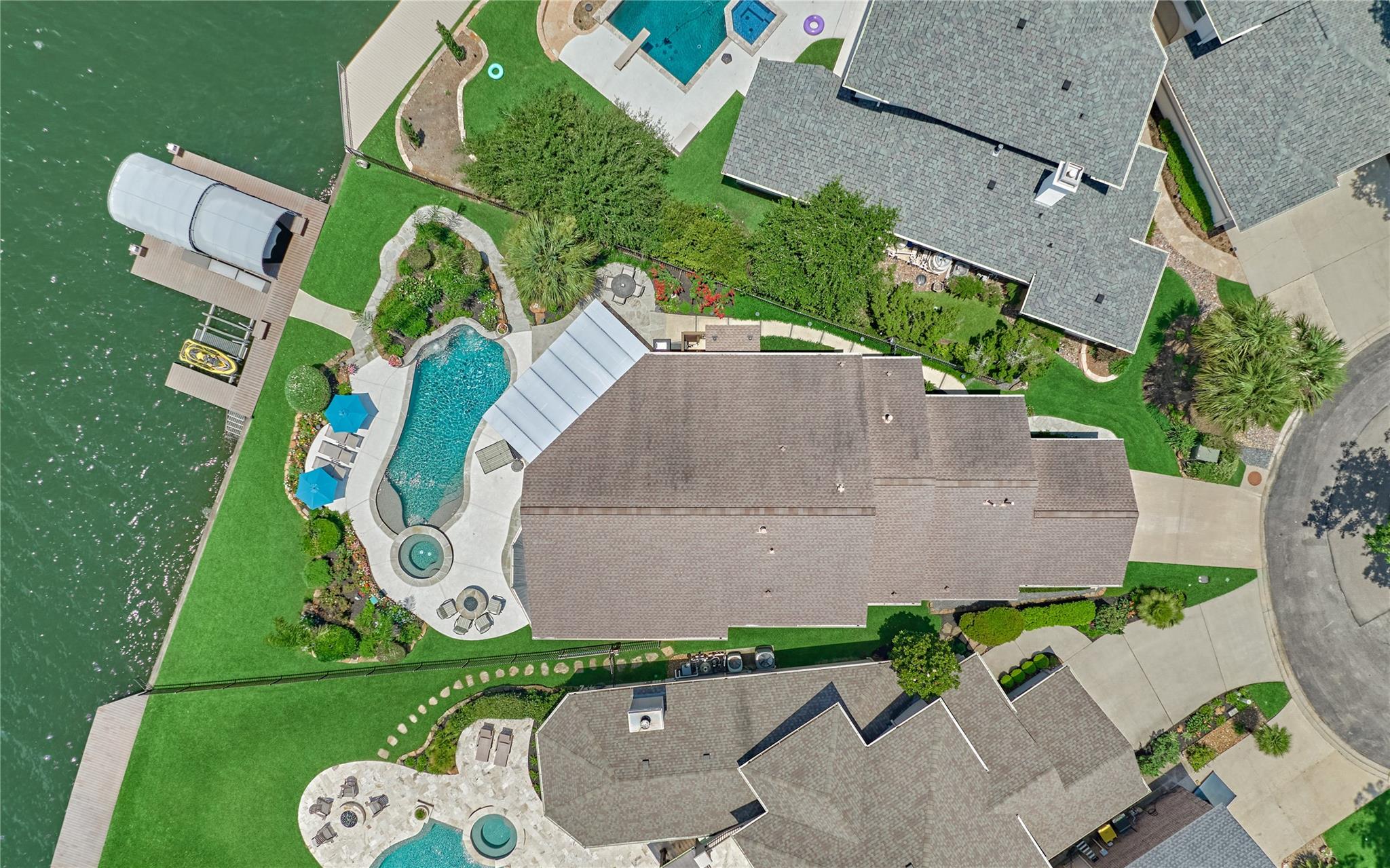 Waterfront home with a backyard pool, spa, landscaped grounds, and dock.