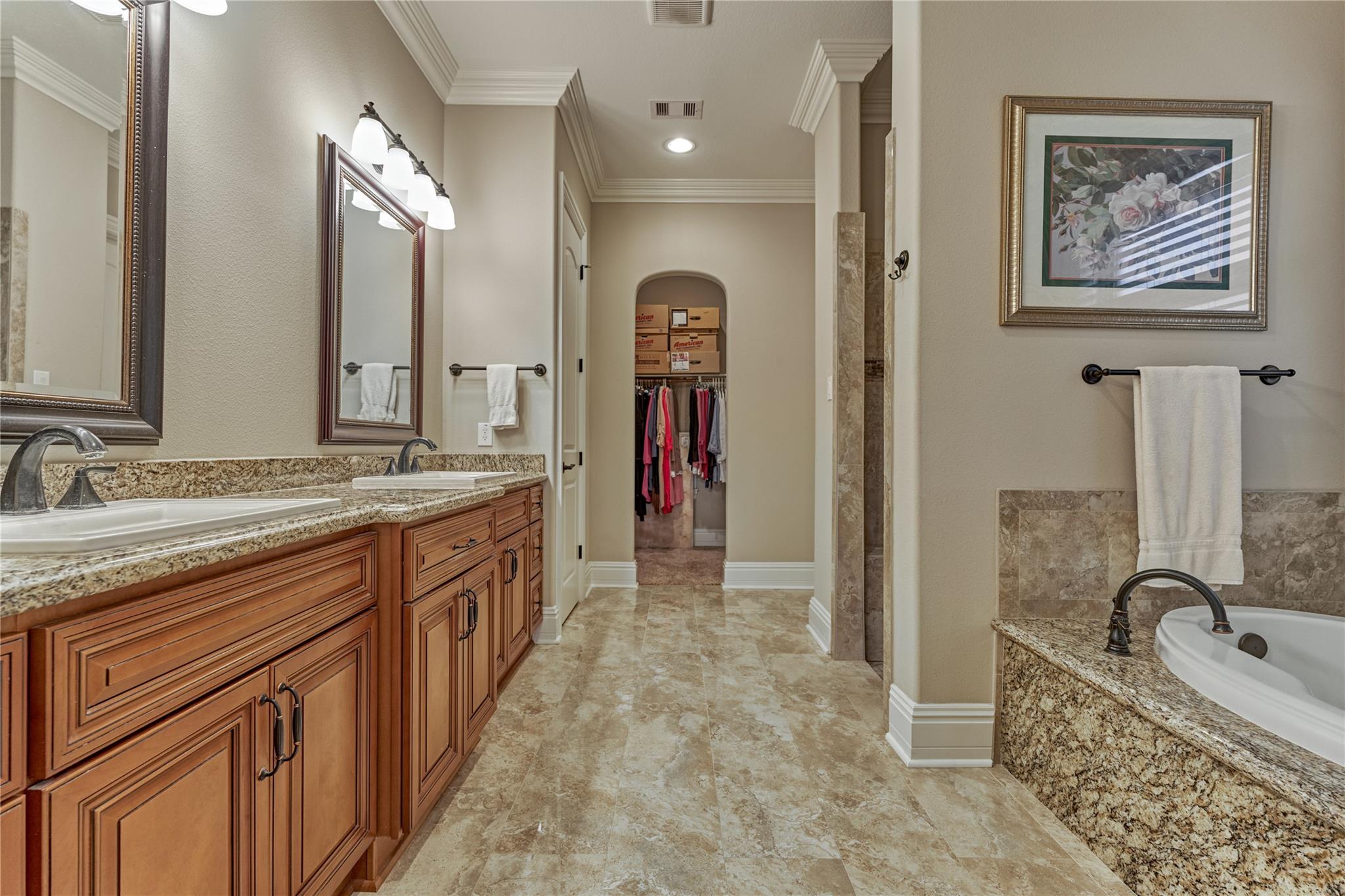 Bathroom with a long wood double vanity and granite counters, a tub, and an open closet beyond.