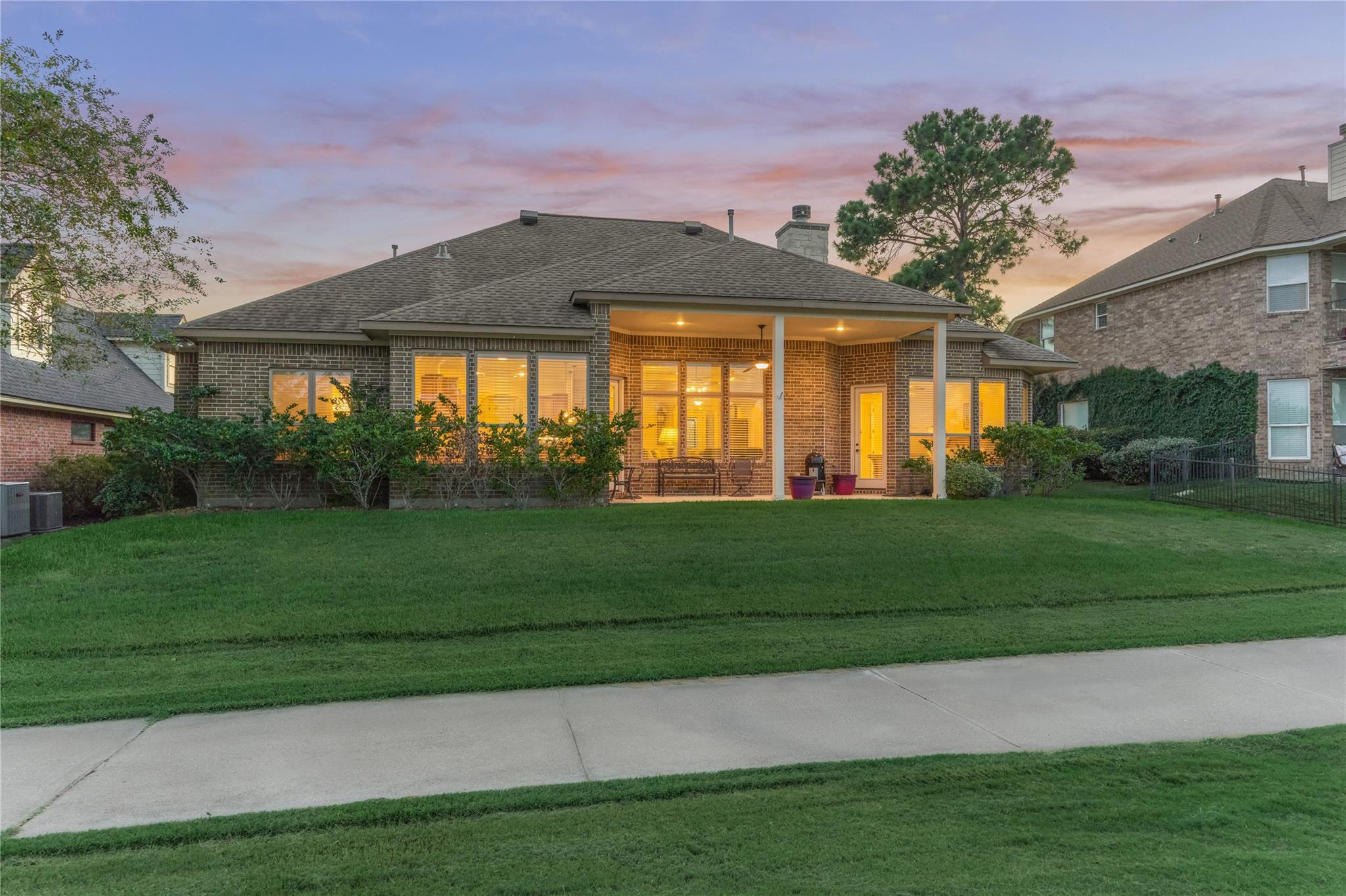 Rear of a brick home at dusk, with a covered patio and warmly lit windows.