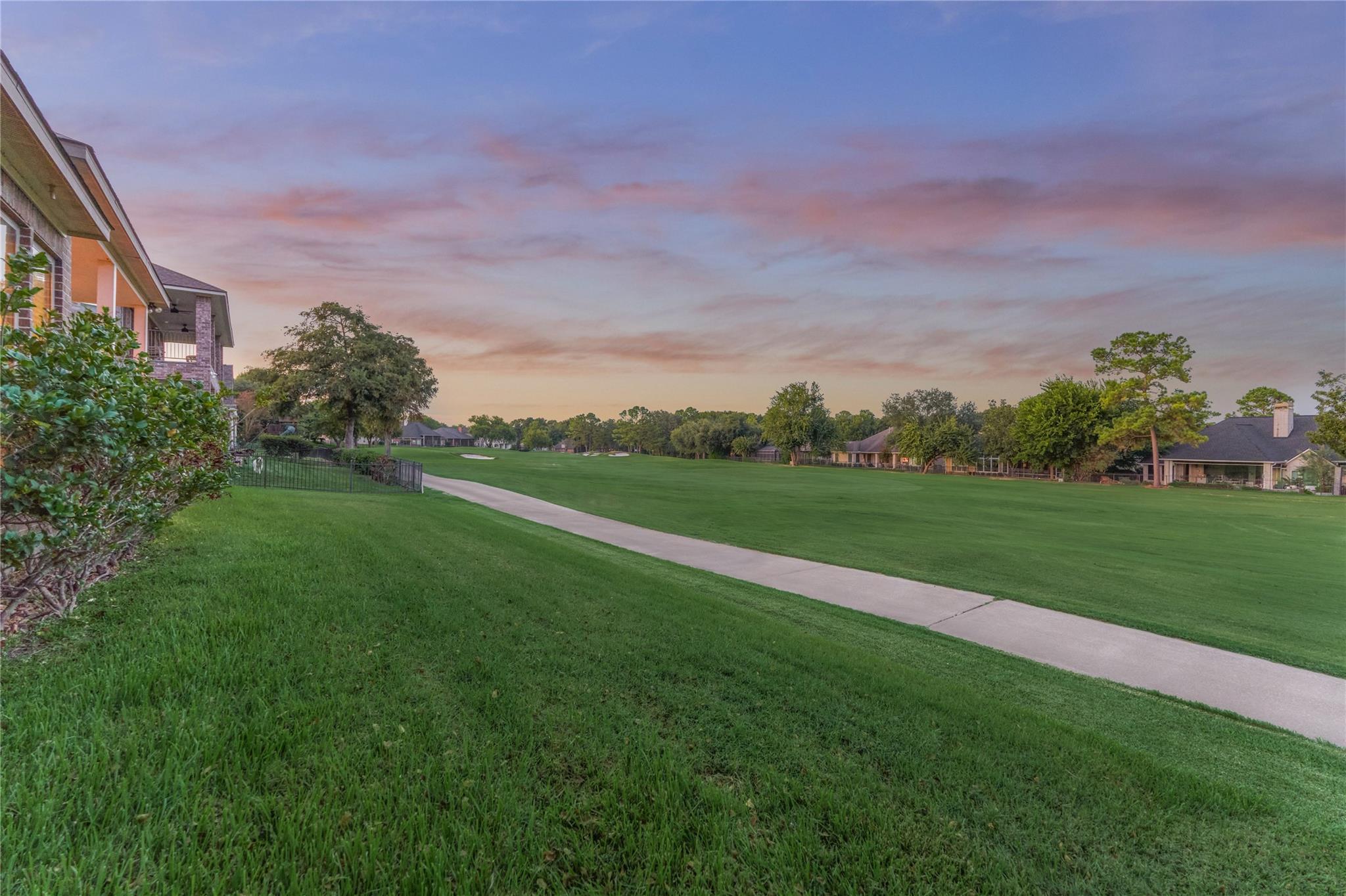 Golf course fairway and winding path beside homes under a pink dusk sky.
