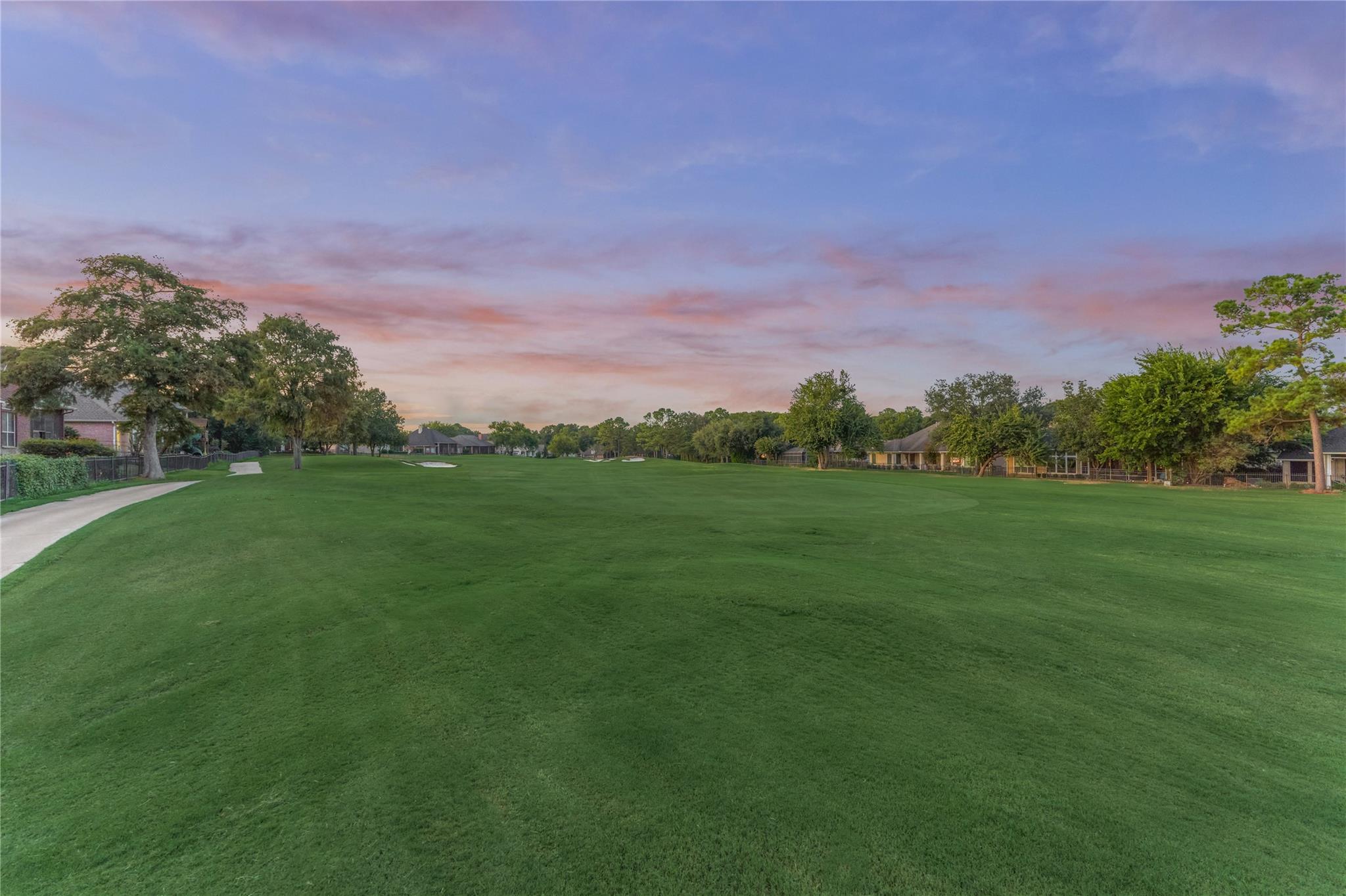 Manicured golf course lawn bordered by homes and trees beneath a pink dusk sky.
