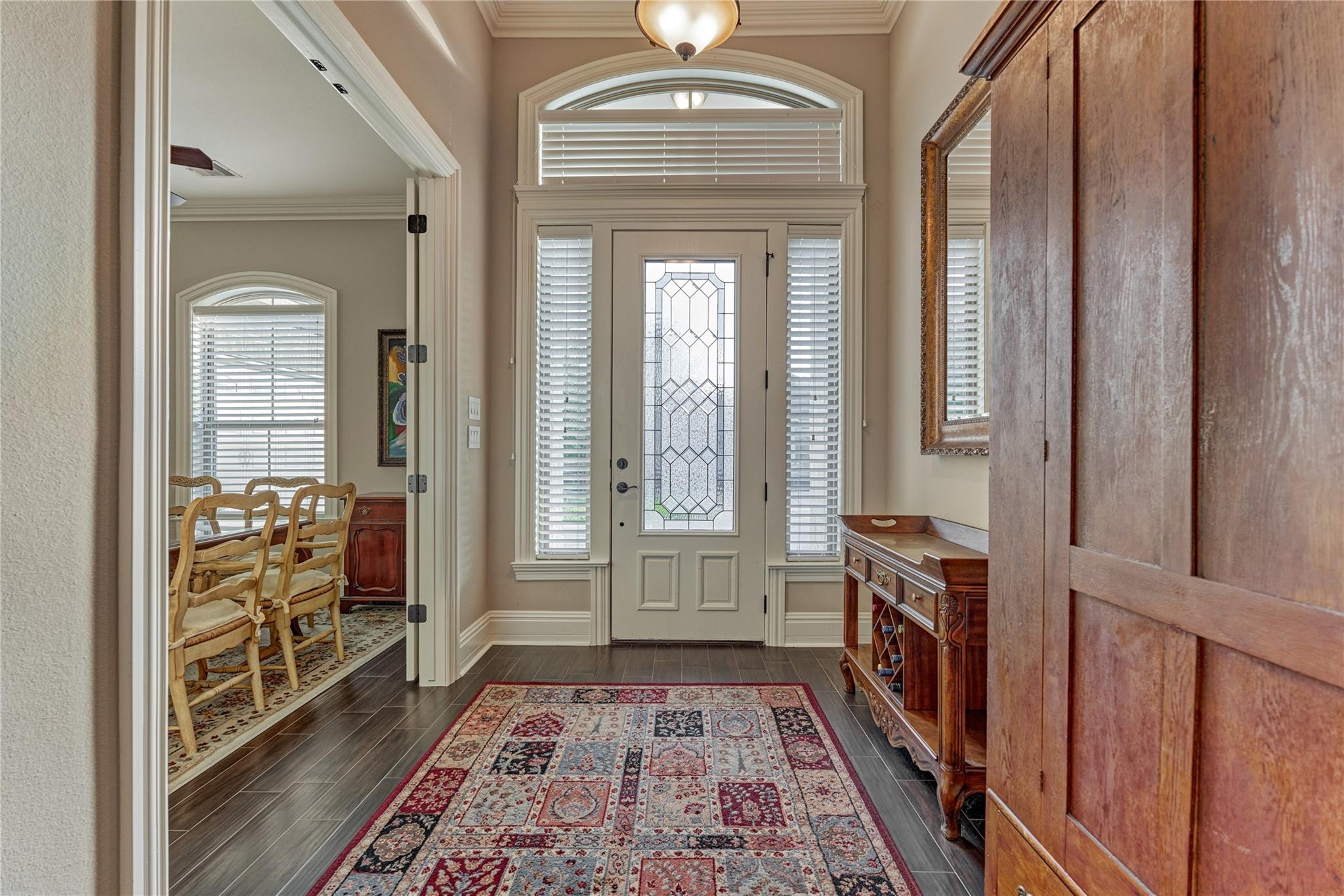 Entry foyer with a decorative glass front door, patterned rug, and wooden console table.