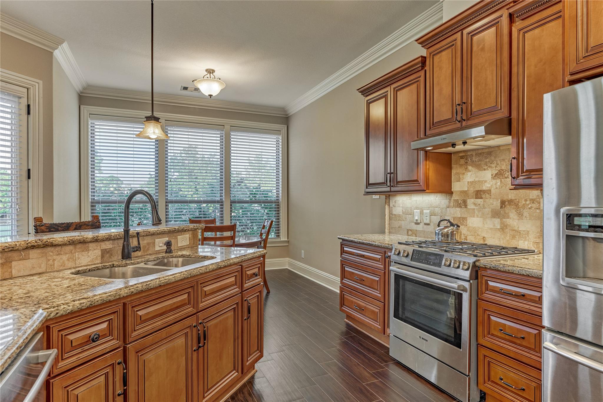 Kitchen with rich wood cabinets, granite counters, a large sink island, and stainless steel appliances.
