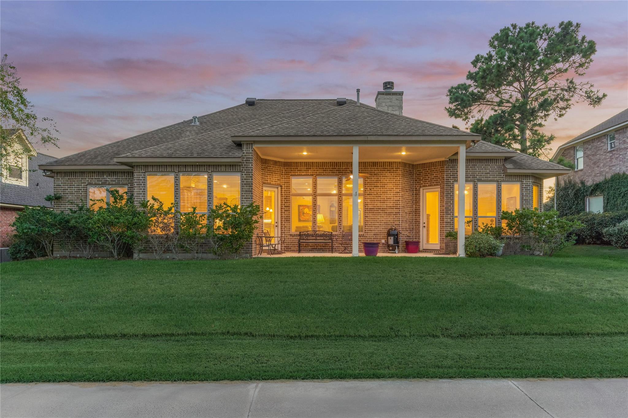 Brick home’s rear exterior at dusk, with a covered patio and warmly lit windows.
