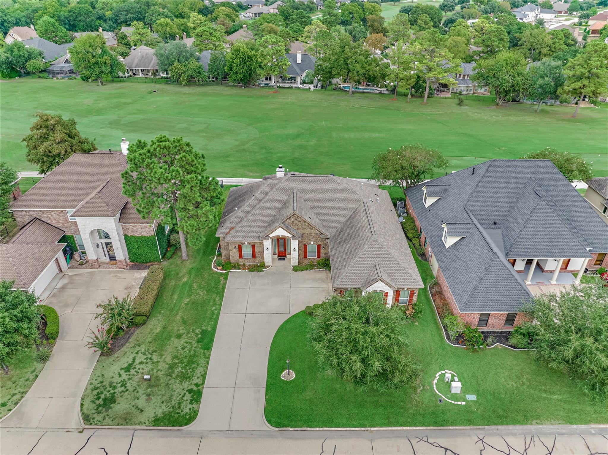 Aerial view of a brick home beside a broad green golf course fairway.