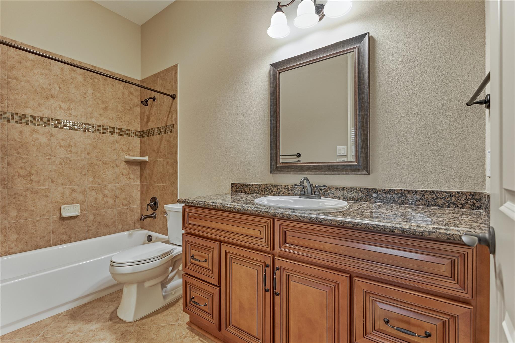 Bathroom with a large wood vanity, granite countertop, and tan tiled tub surround.