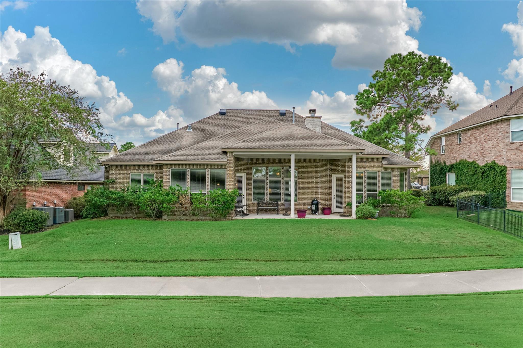 Brick house with a covered rear patio overlooking a broad green lawn.