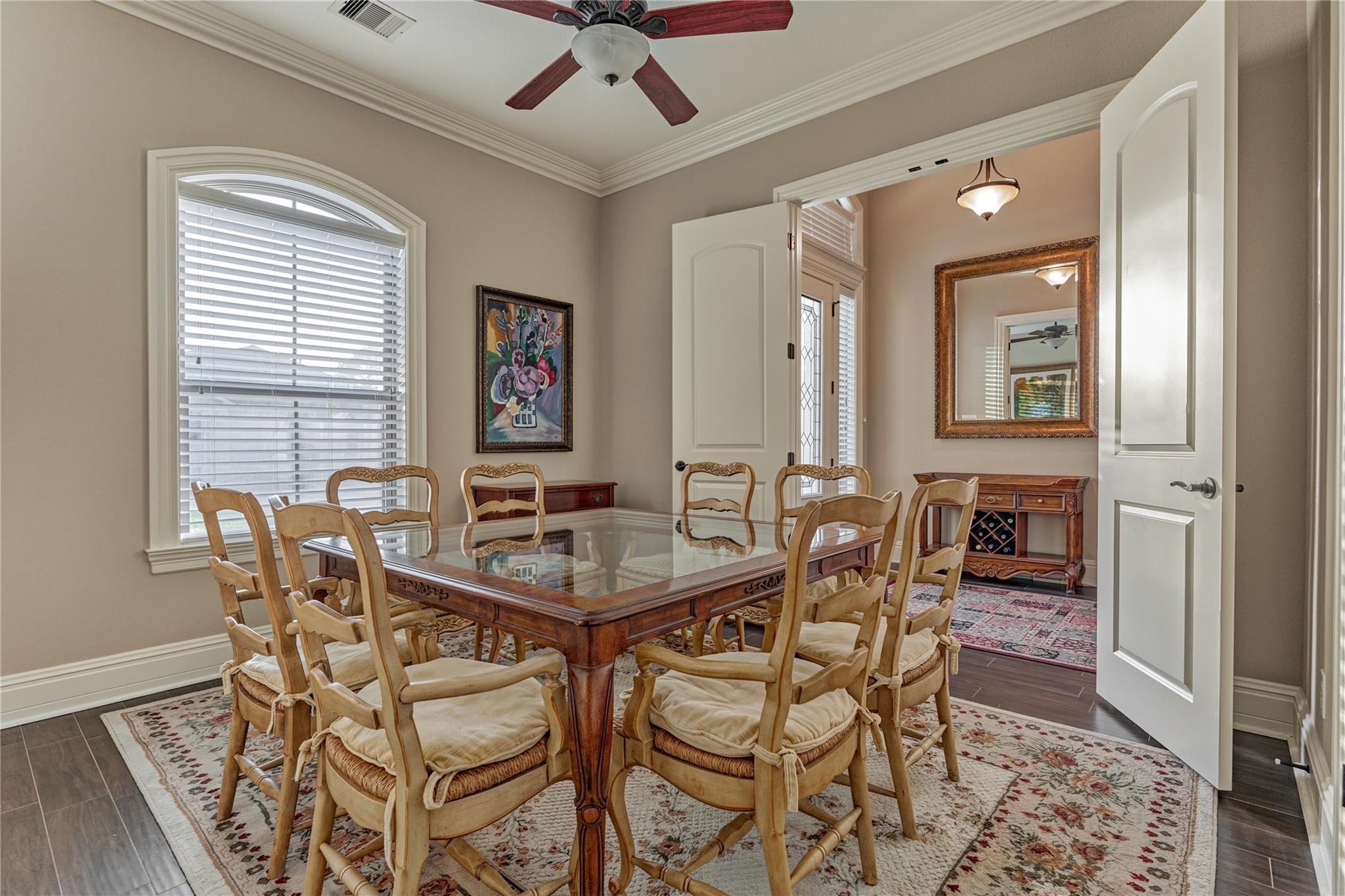Dining room with a glass-top wooden table, carved chairs, and open doors to an adjoining room.