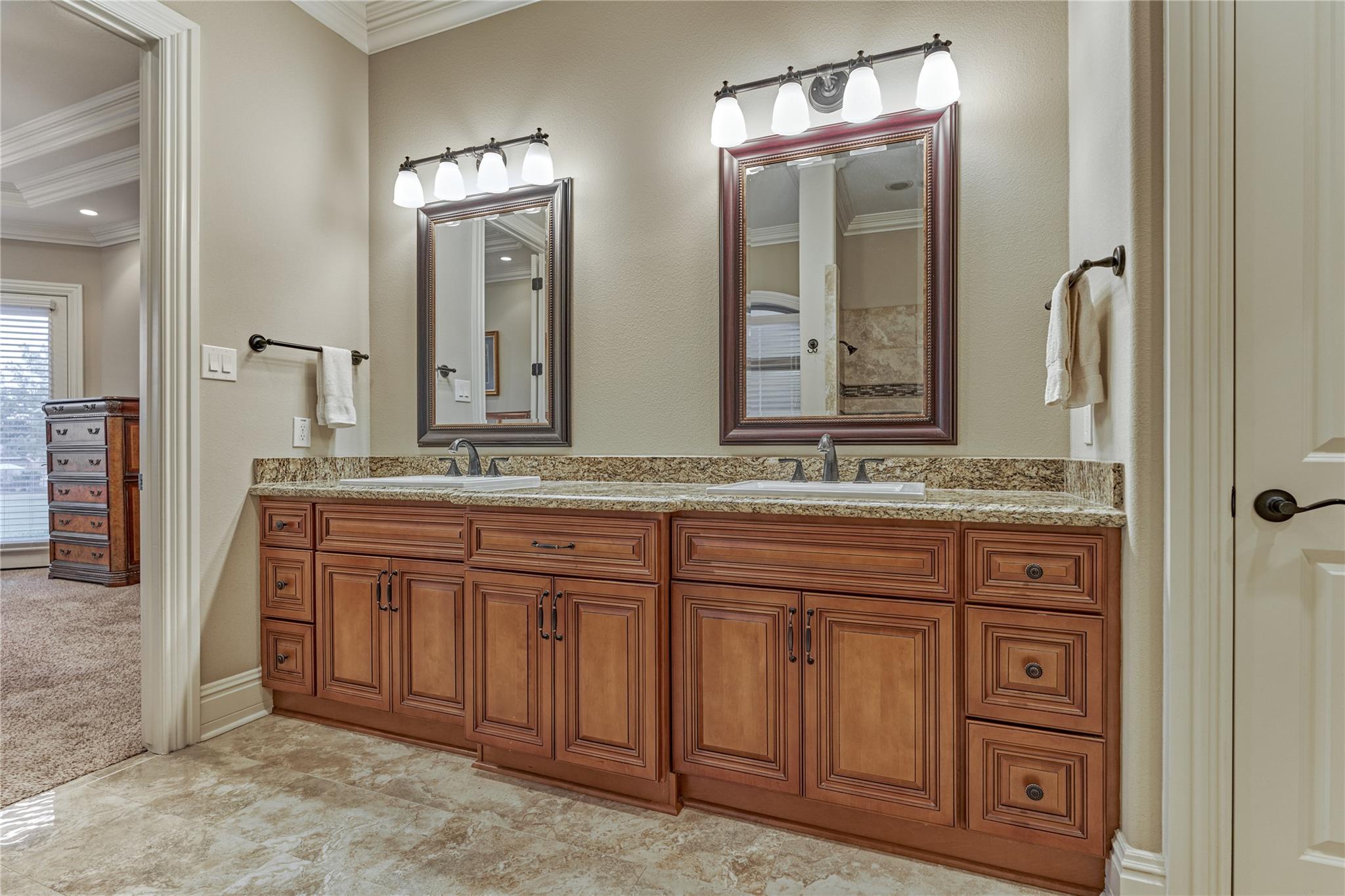 Bathroom with a double-sink vanity, warm wood cabinets, granite countertop, and two framed mirrors.