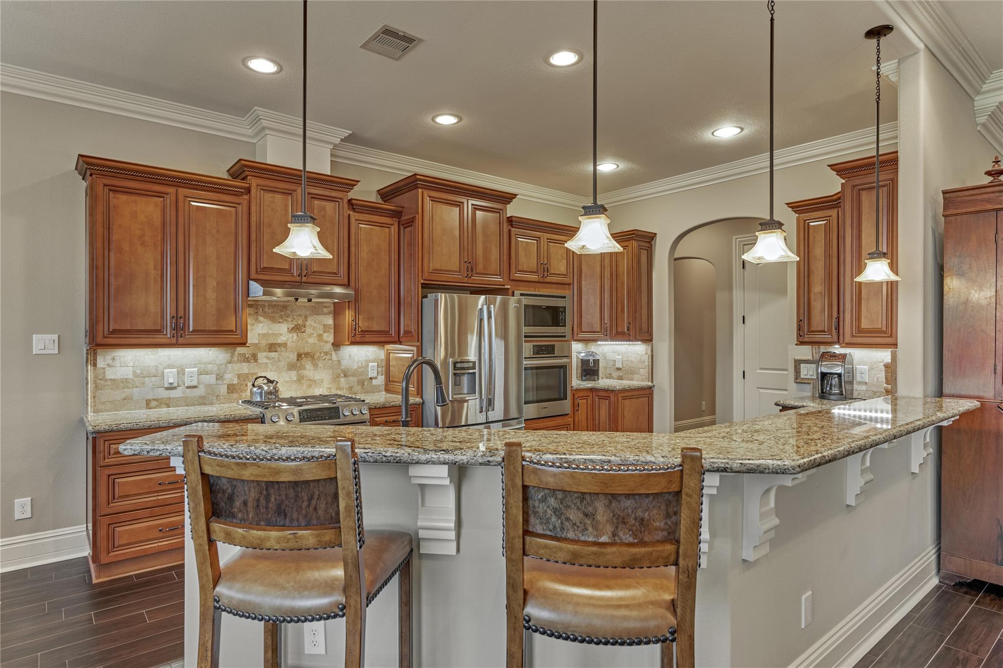 Kitchen with wood cabinets, granite breakfast bar, two stools, and stainless steel appliances.