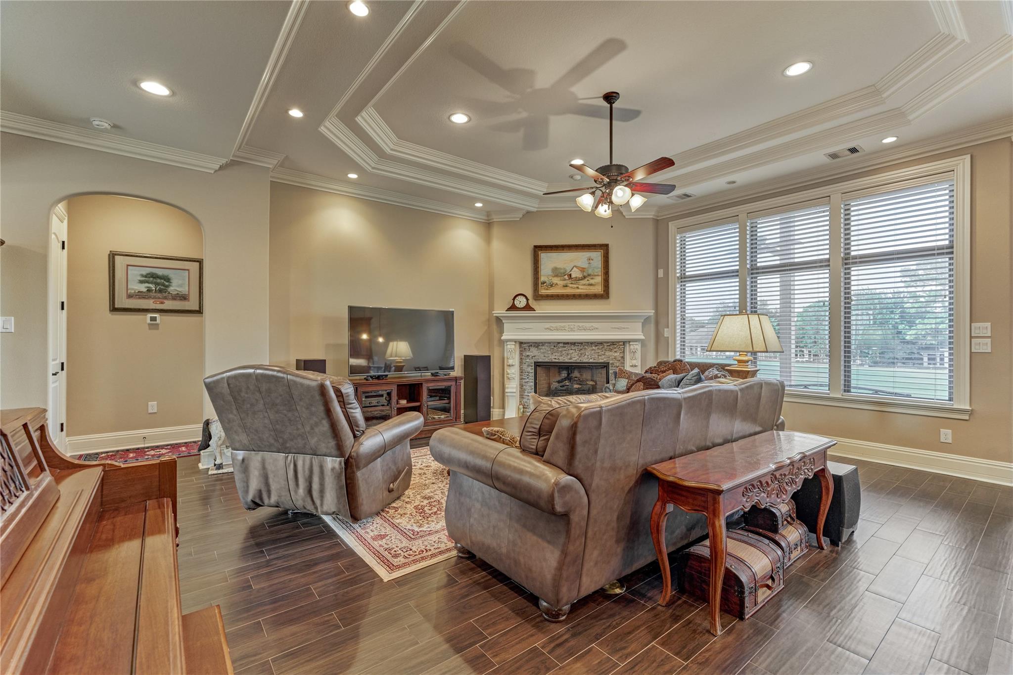 Living room with leather seating, a white-mantel fireplace, large windows, and a tray ceiling.