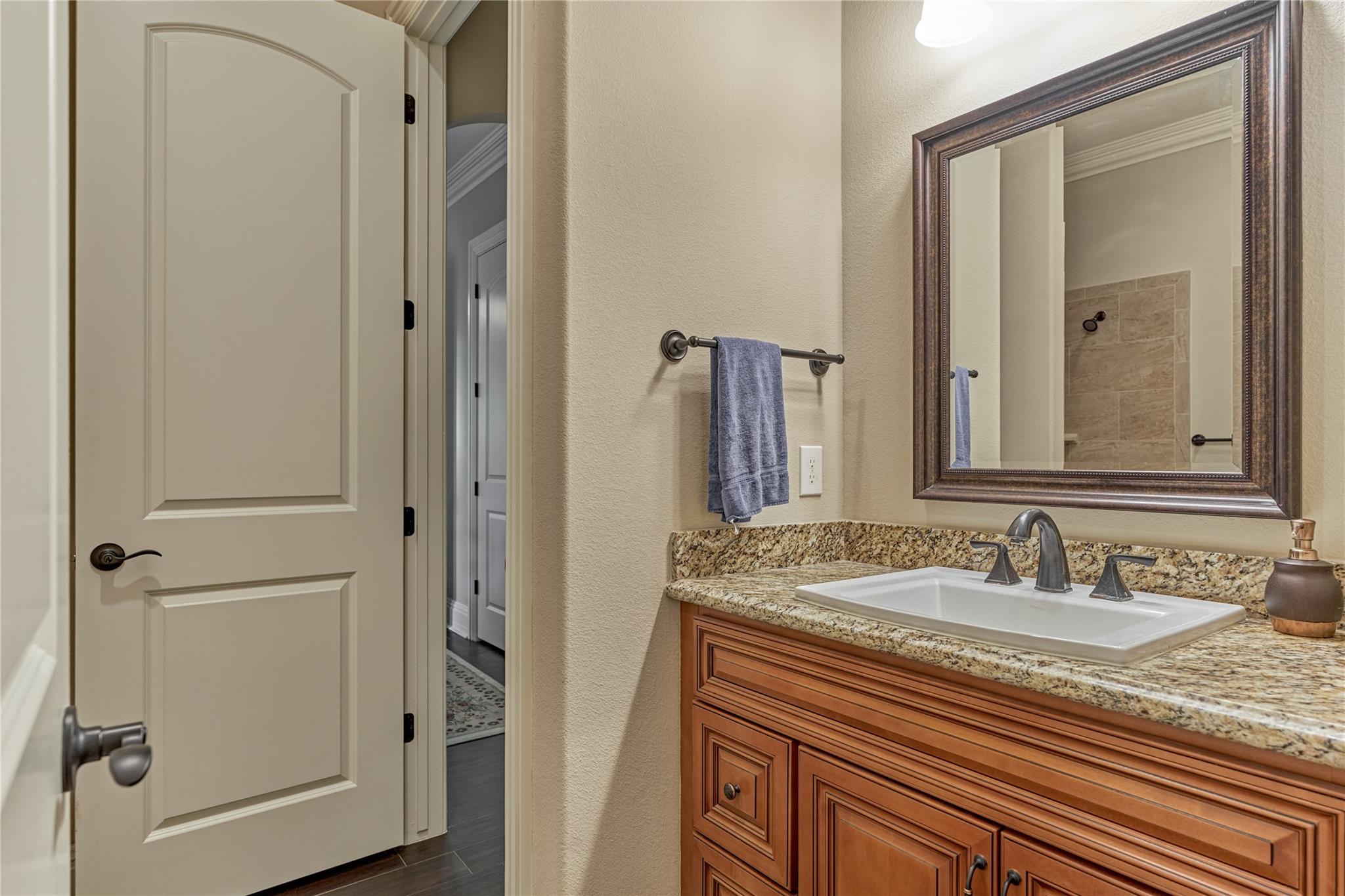 Bathroom vanity with a white sink, granite countertop, wood cabinets, and framed mirror.