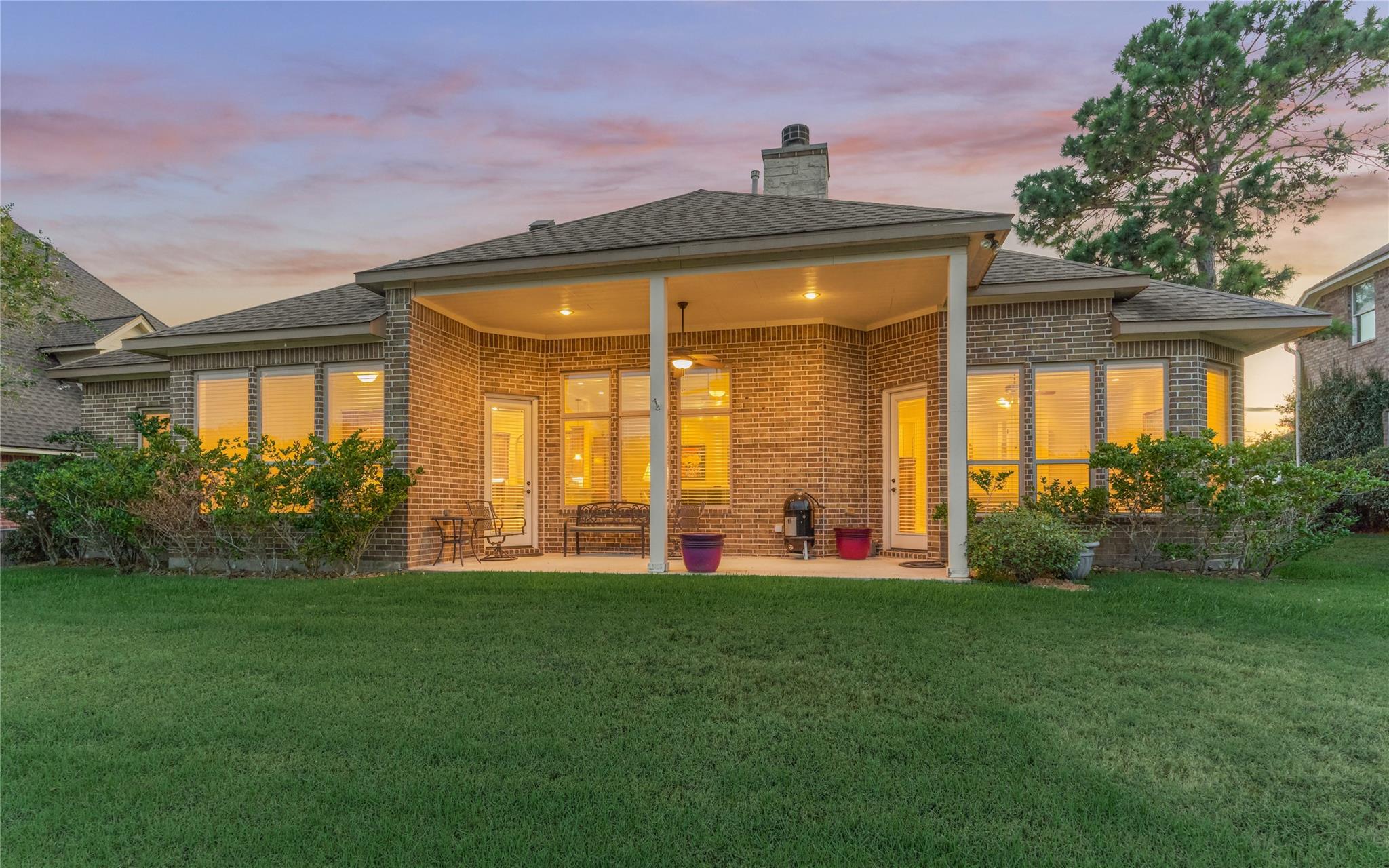 Brick home’s rear exterior at dusk, with a covered patio and broad green lawn.