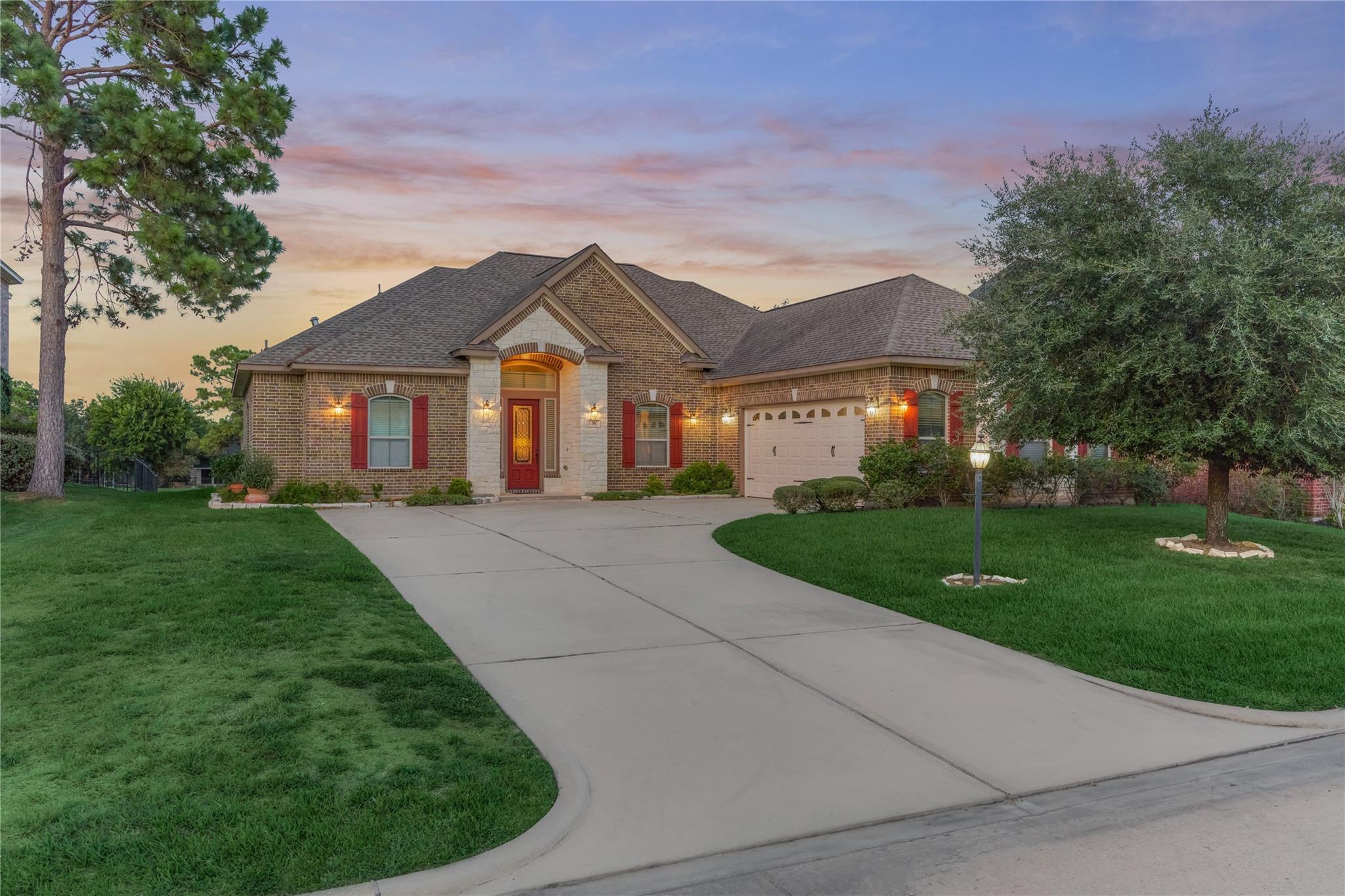 Brick house at dusk with a red front door, attached garage, and curved driveway.