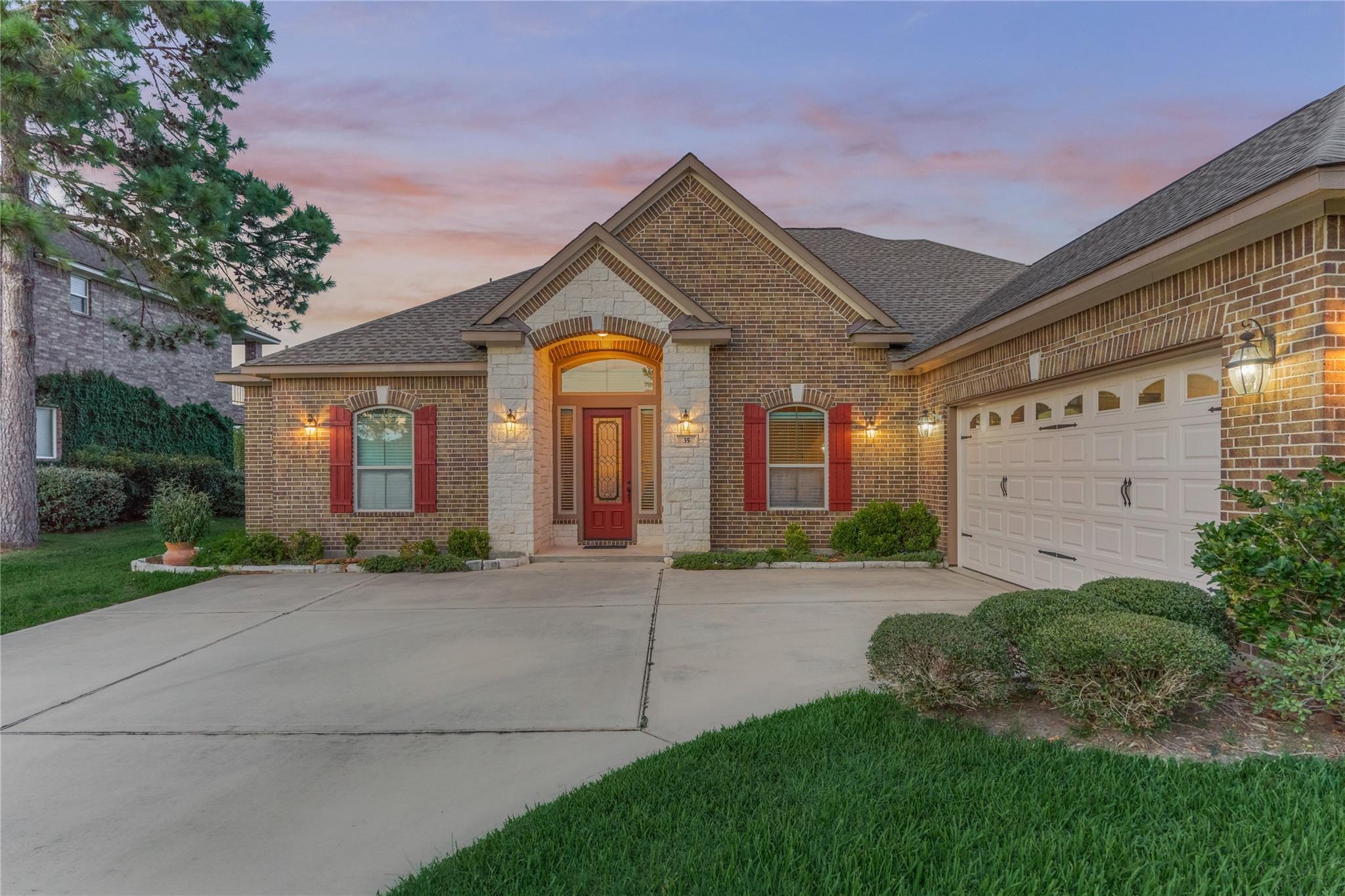 Brick home exterior at dusk with a red front door, stone entry, and attached garage.