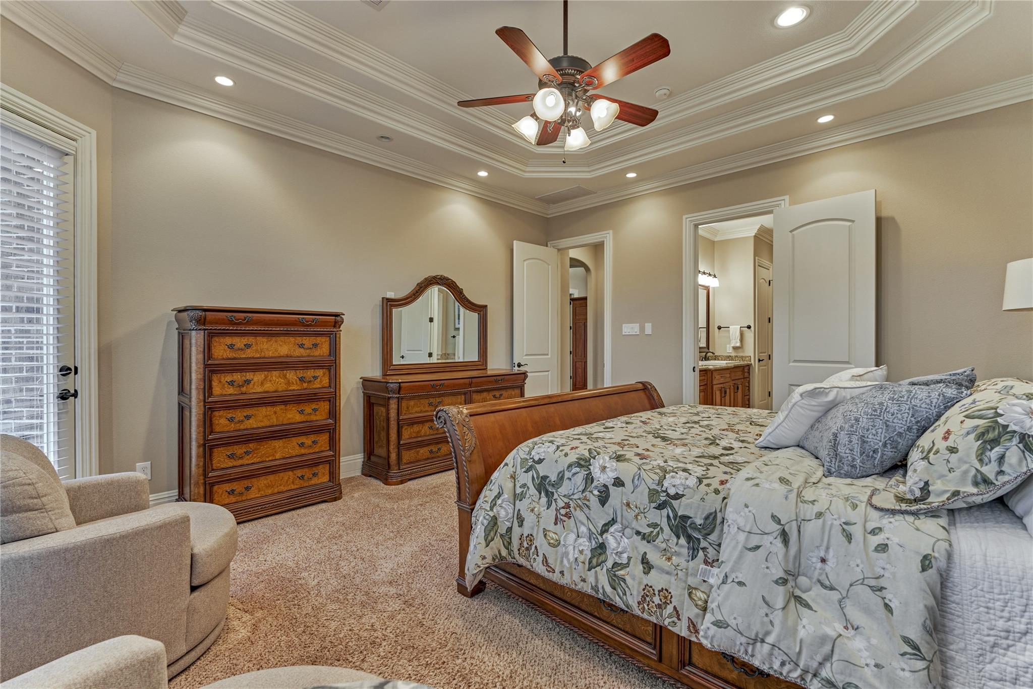 Furnished bedroom with a carved wooden bed, floral bedding, matching dresser, and tray ceiling.